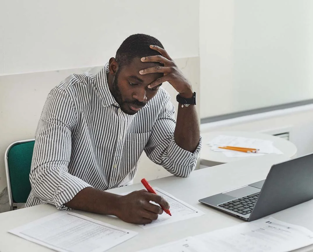 Concerned man carefully reviews reports at his desk covered in stacks of paper work.