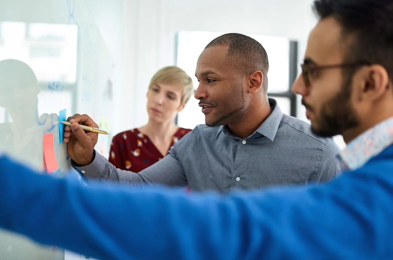 three-coworkers-carefully-looking-at-whiteboard-while-one-of-them-makes-a-note-on-it