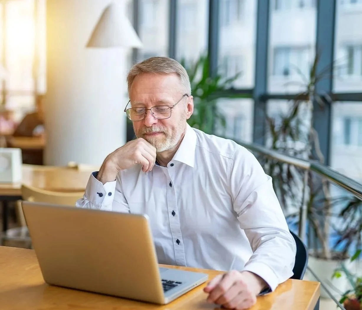 man reviewing information on his laptop and taking notes in plant-filled office space
