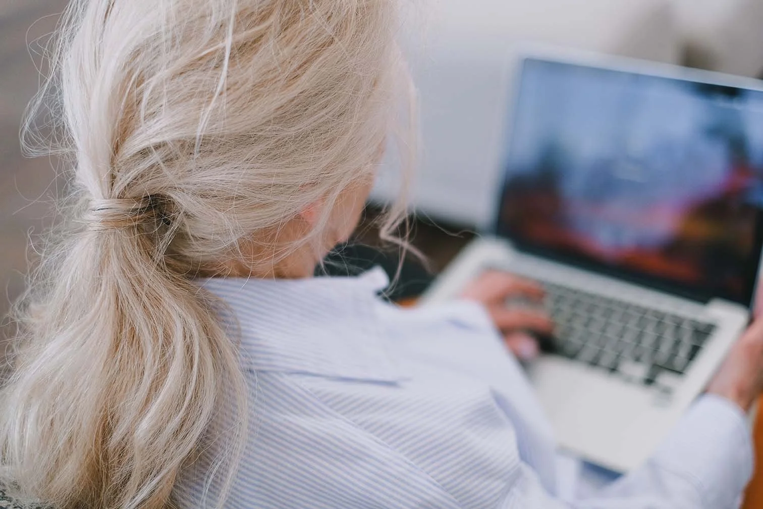 Nonprofit executive in blue stripped shirt posting about job opportunity on her laptop.