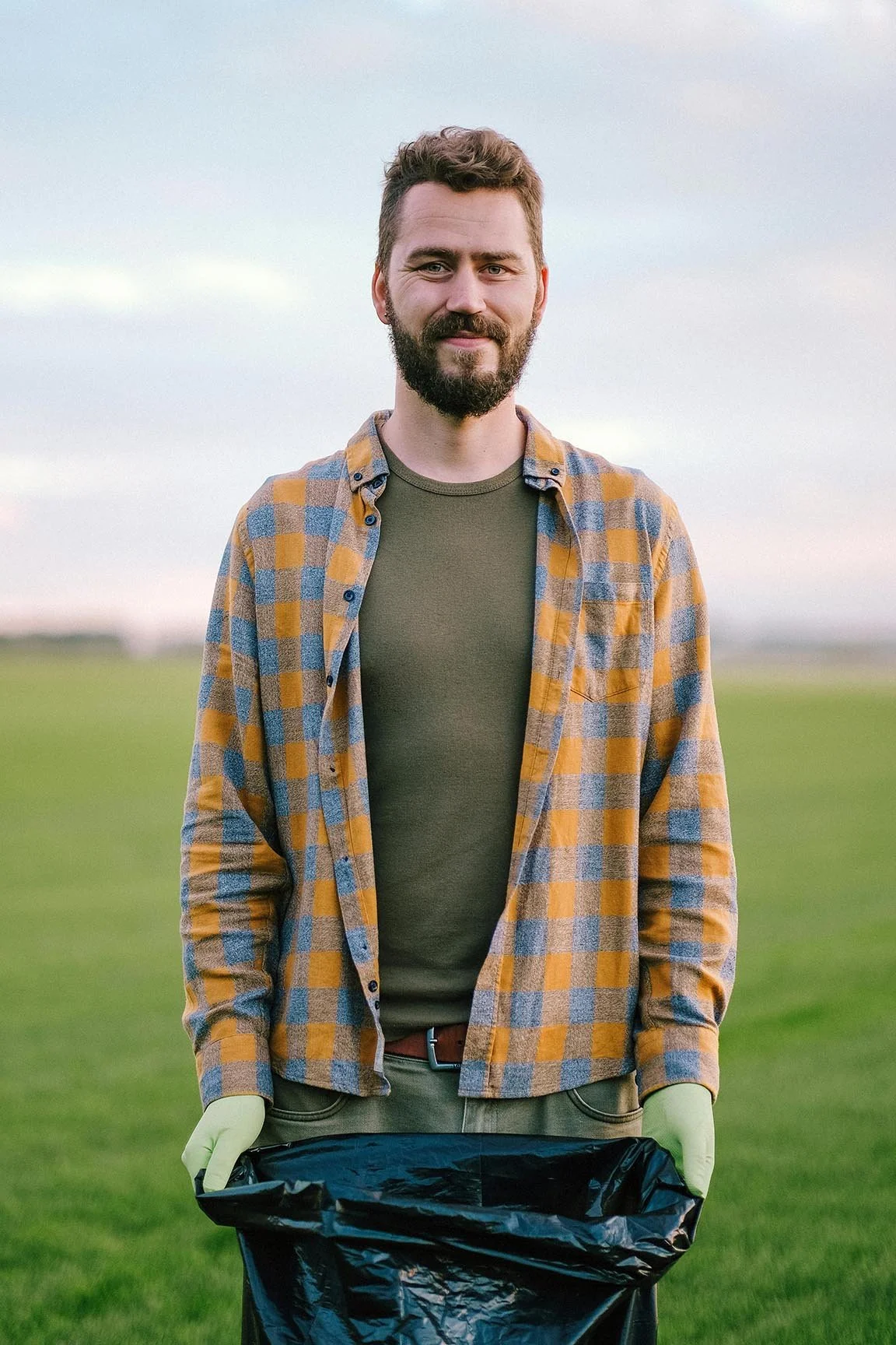 man standing in green field holding open a black trash bag at corporate social responsibility event
