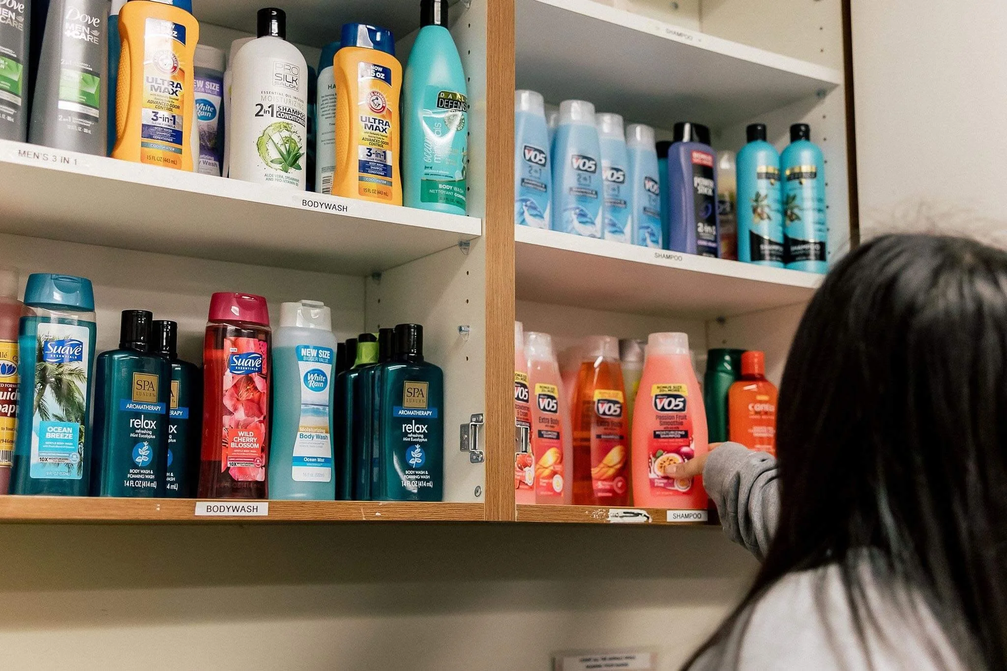 student selecting shampoo from the monarch school's cabinet of community resources in the on-health station