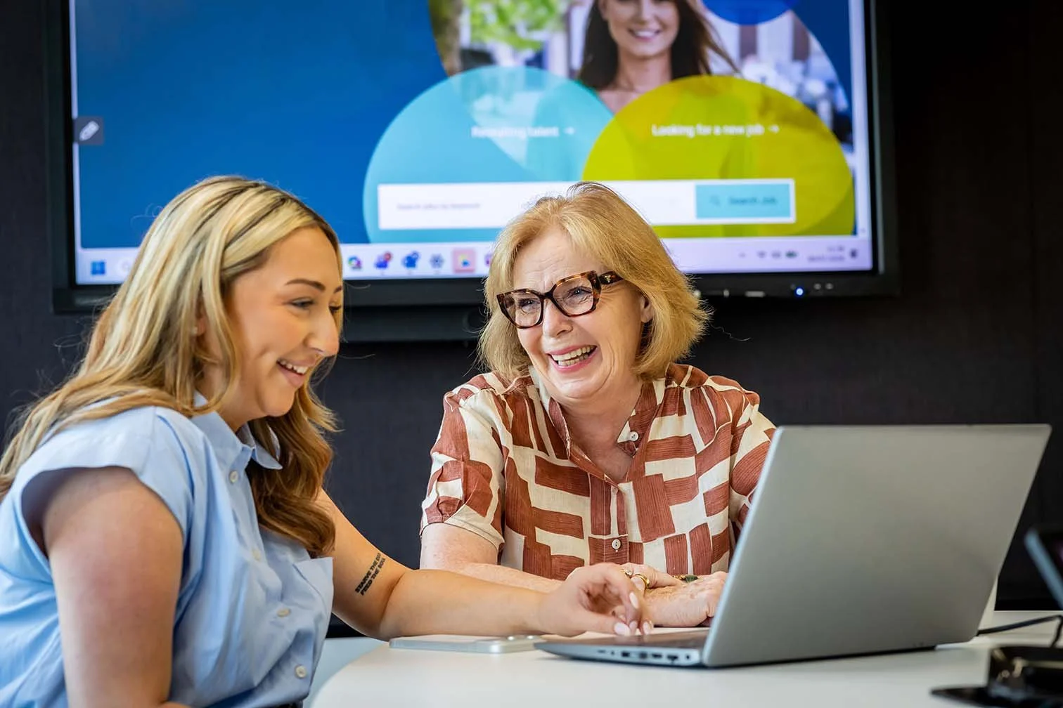 Two nonprofit board members talking while reviewing monthly accounting report on a laptop together in a meeting room.