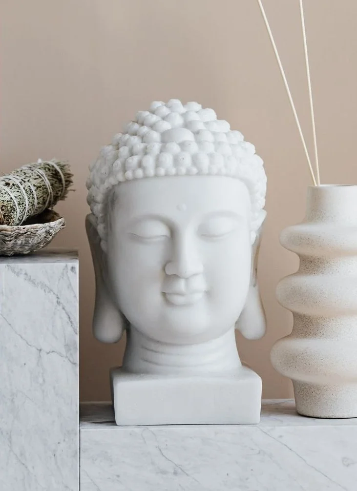 White bust of a Buddha with closed eyes, set on a marble surface.