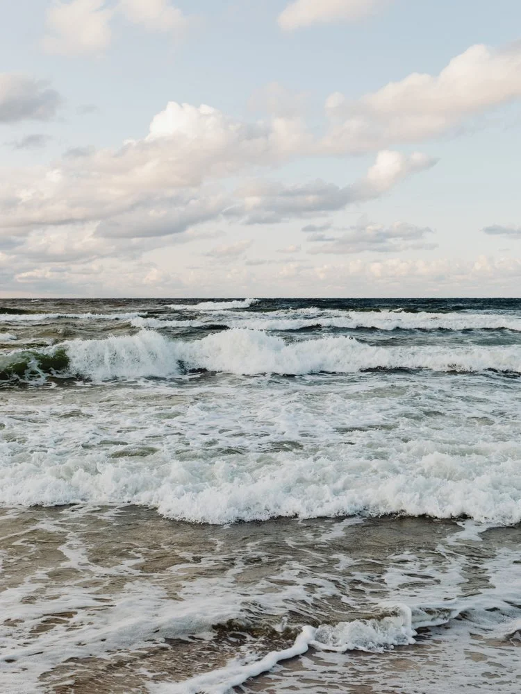 Beach with ocean waves crashing onto the shore under a partly cloudy sky.