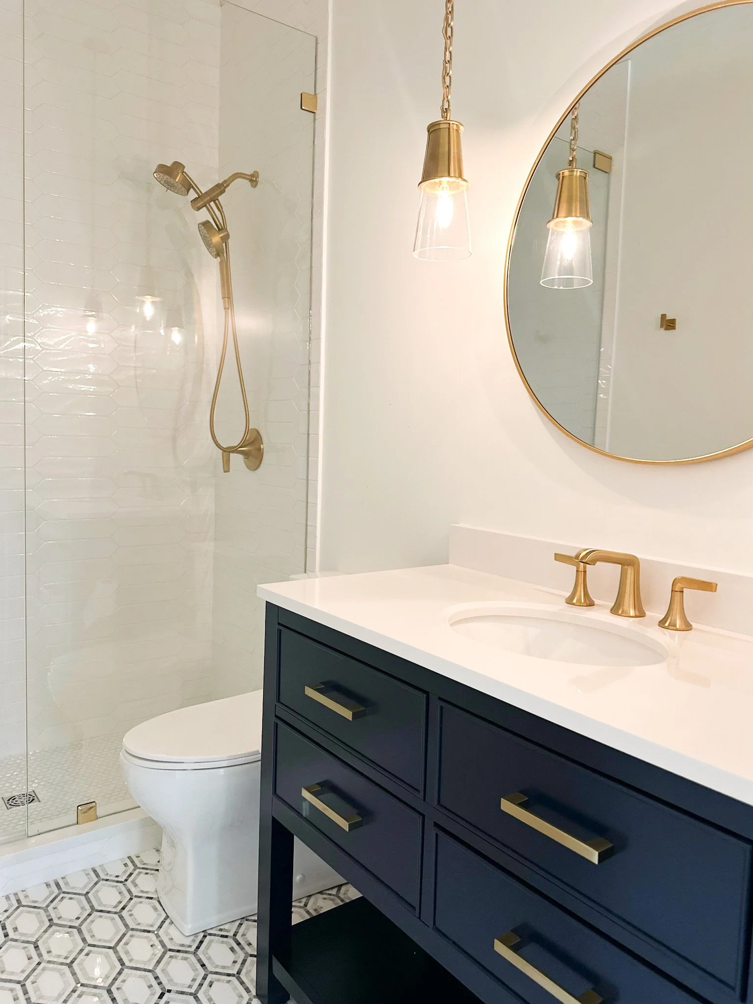 Coastal cool bathroom with navy blue vanity, brass pulls, and geometric shower tile by Lark and Soul interior design.