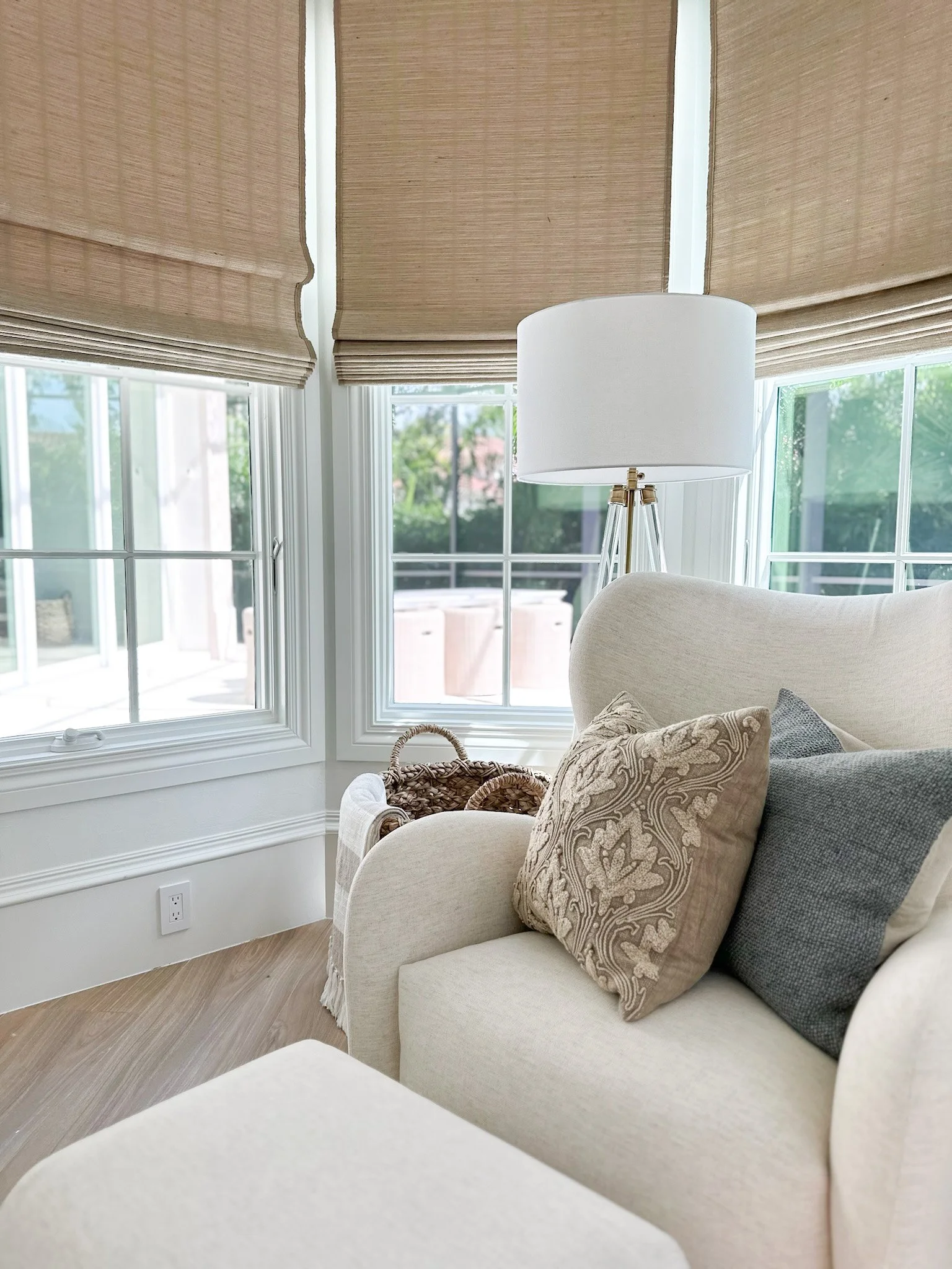 White chair with coastal pillows in front of three windows featuring custom linen roman shades in a Naples home.