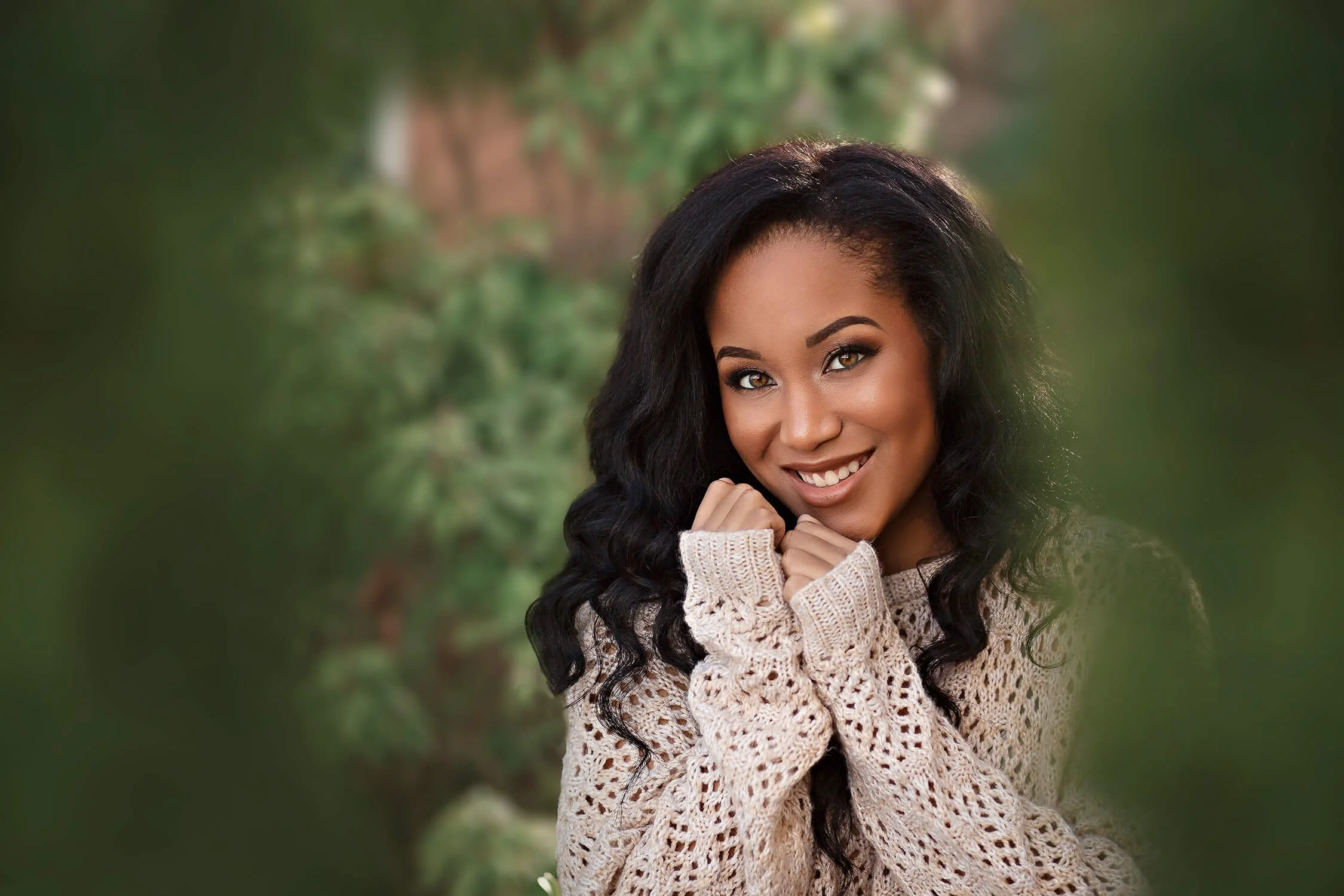 Woman smiling in cream sweater posing outside near trees