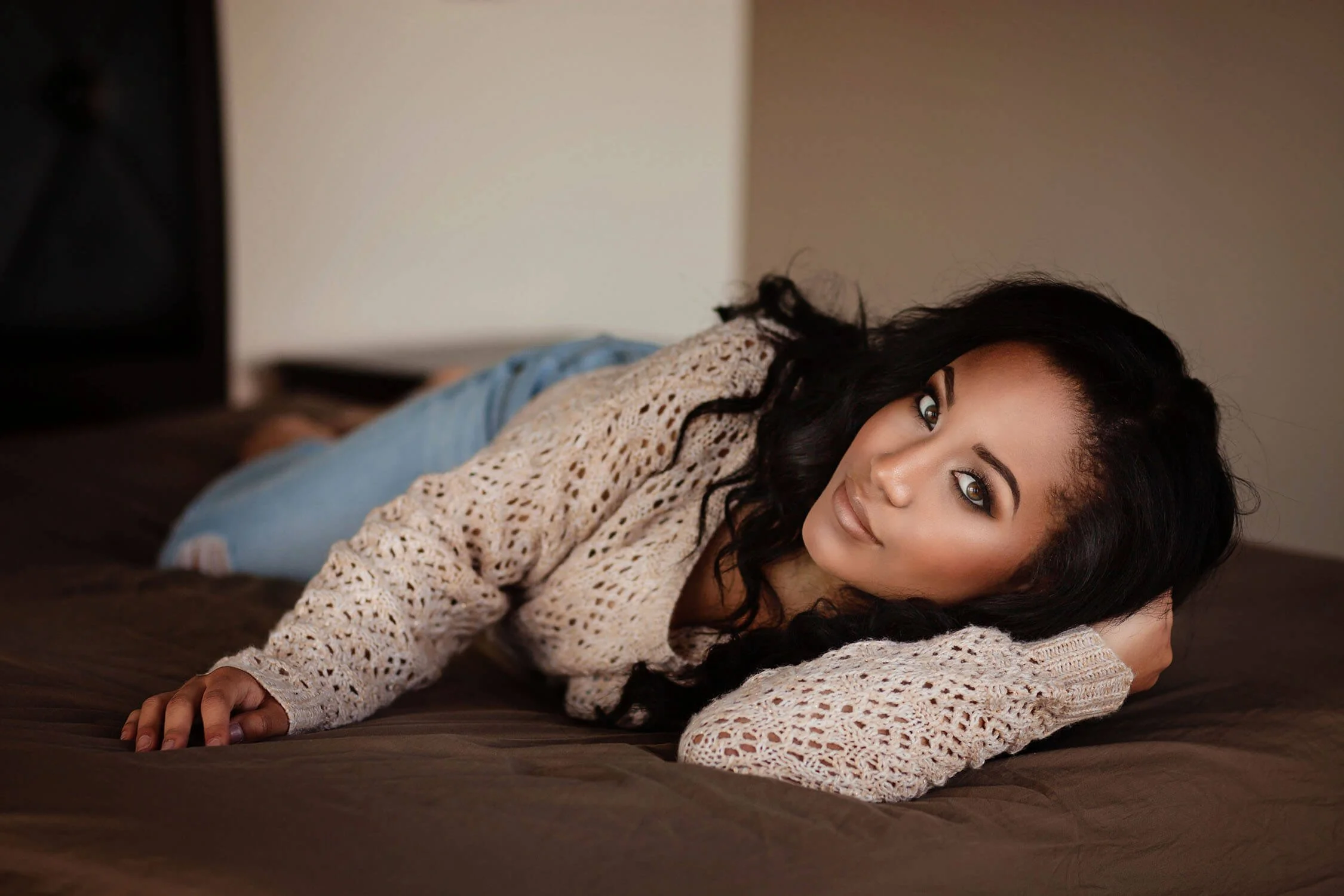 Woman posing on a bed in a casual covered outfit during a boudoir session