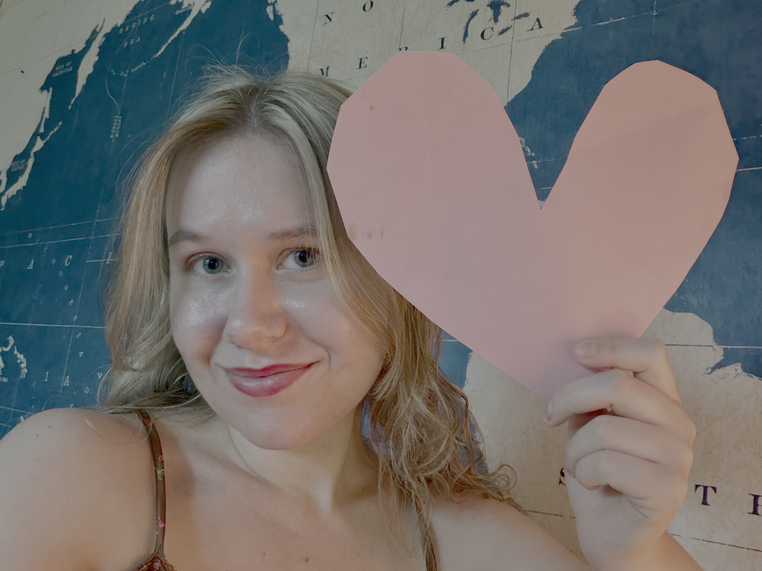 Smiling woman holds pink paper heart. 