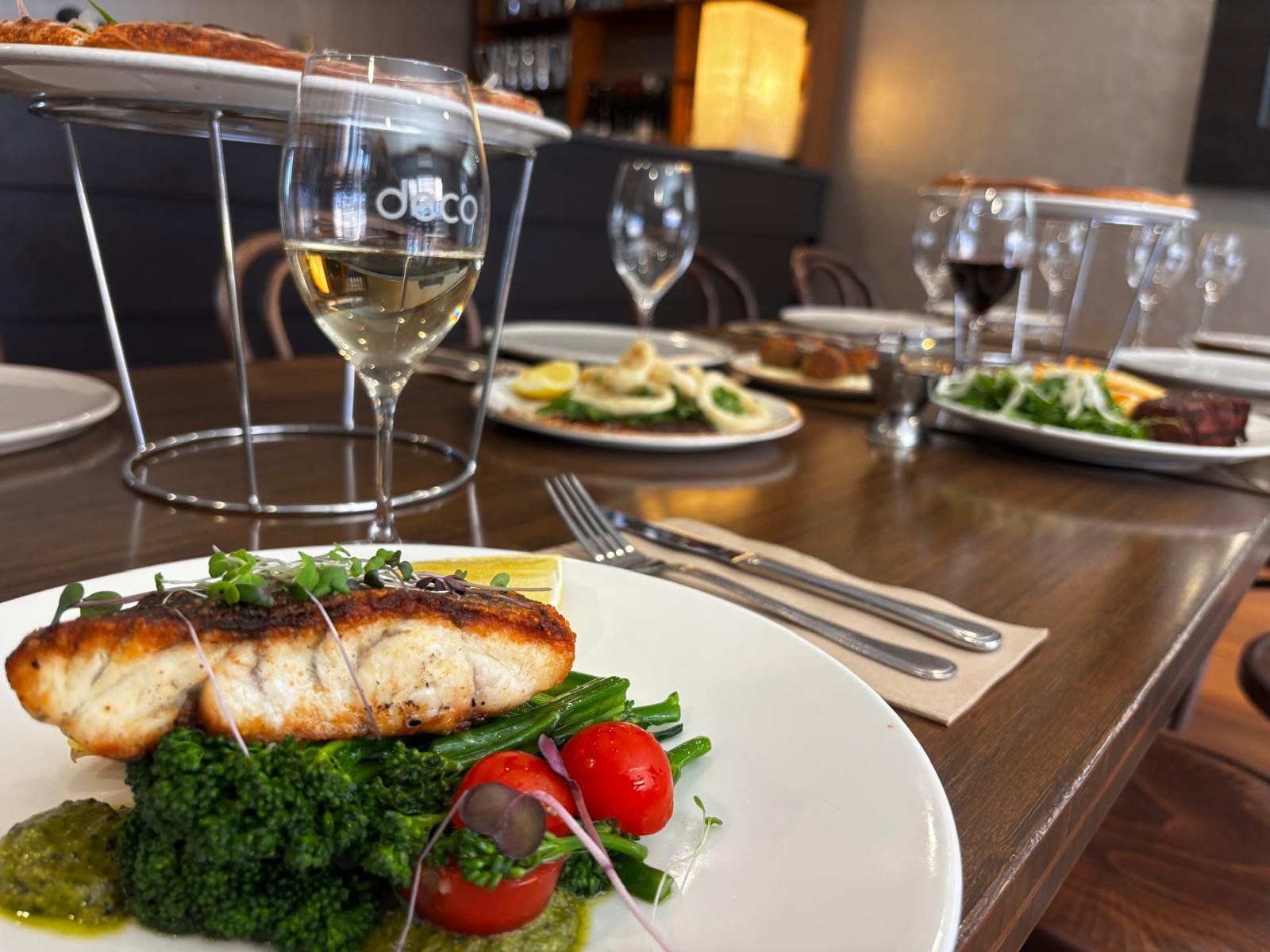 A dinner table with plates of grilled fish, salad, and vegetables, along with glasses of white and red wine.
