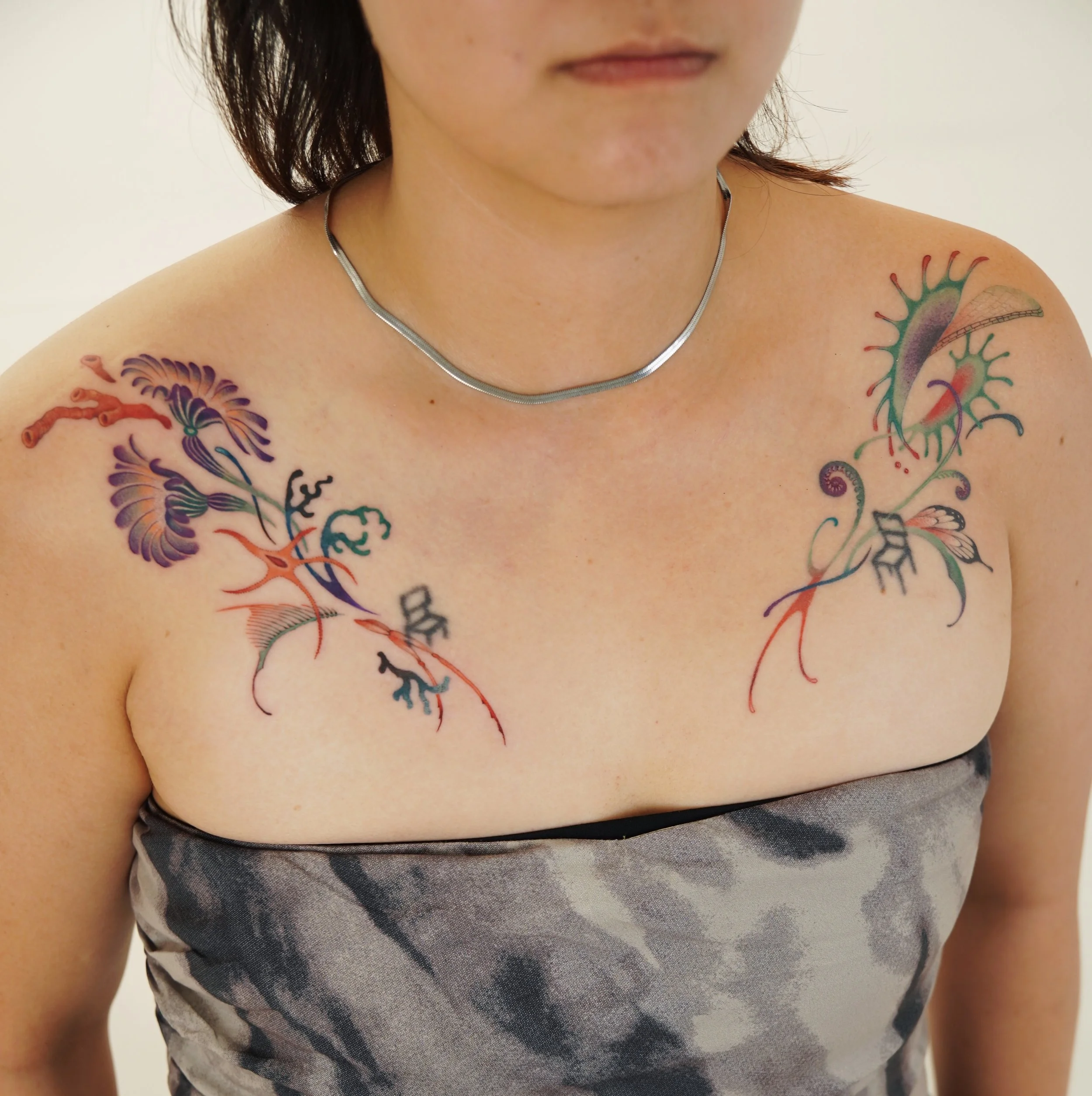 Tattoo of a paper bird with a blue floral pattern, rain cloud above it with brown shading and blue raindrops