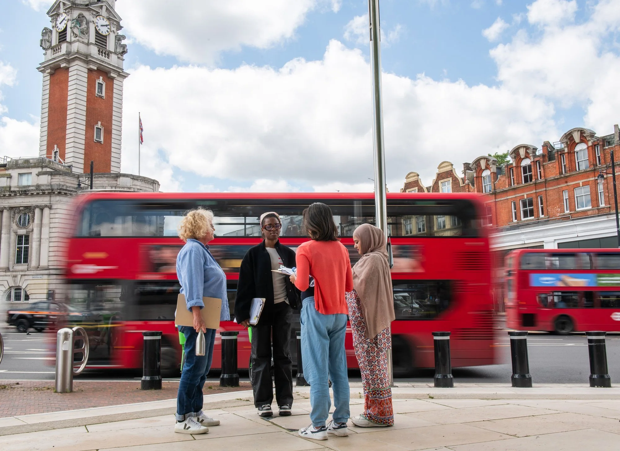four community researchers in front of Lambeth Town Hall, with a red London bus passing by