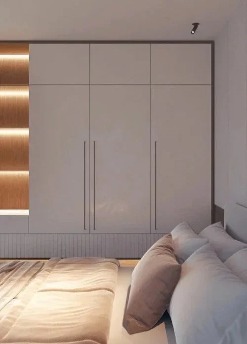 Soveværelse med et stort hvidt skab, seng med puder, træversion af vægdekoration og en loftlampe.