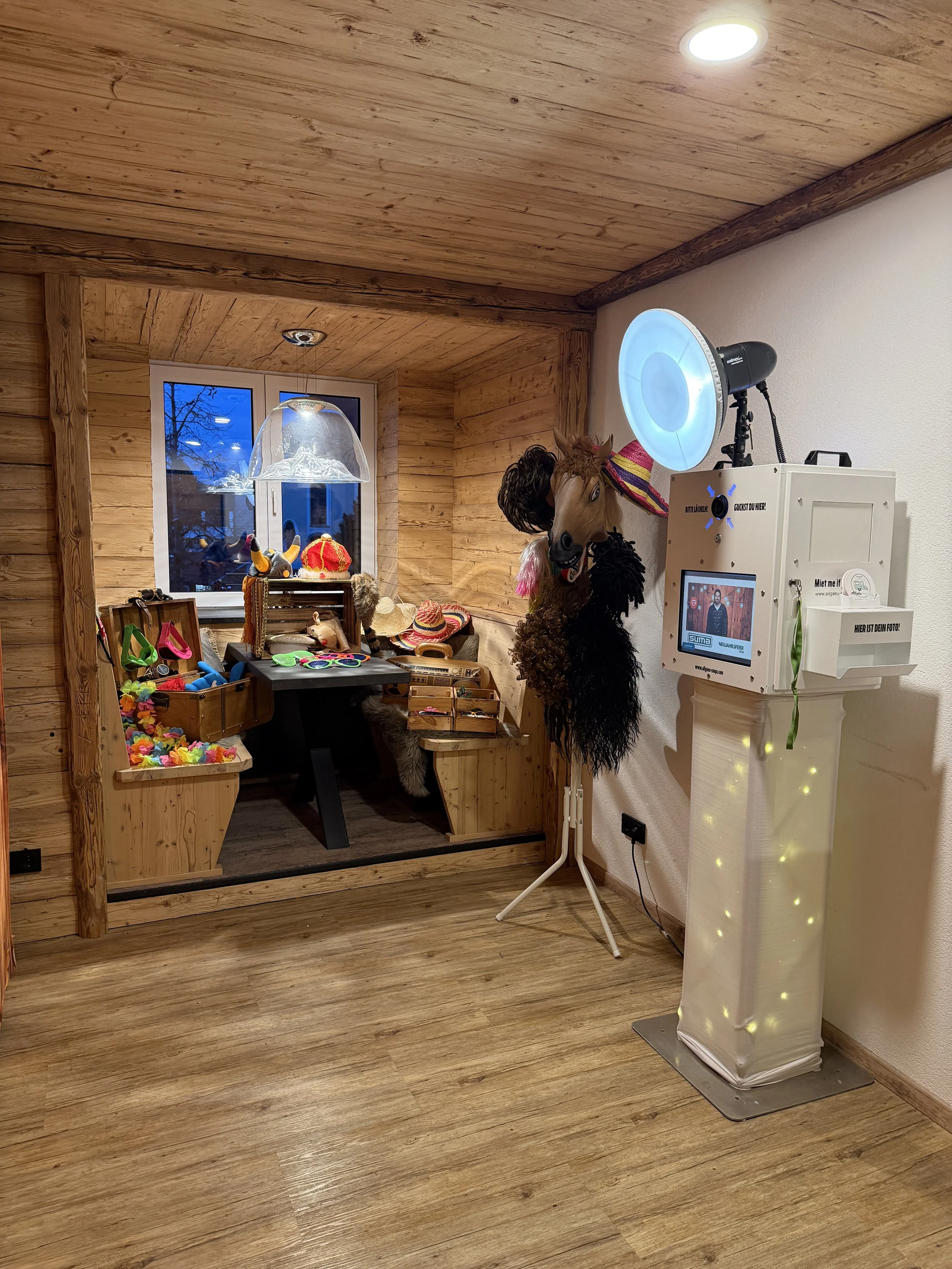 Fotobooth mit Kostümen und Zubehör für Fotos, im Hintergrund eine Holzvertäfelung und ein Fenster, vorne ein Cowboy-Hut und ein Pferdekopf-Standbild, Beleuchtungsausrüstung.