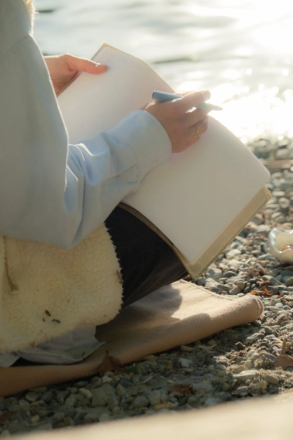 Jil Bianca journaling by the water, representing creative practices like collage making, painting, and reflection.