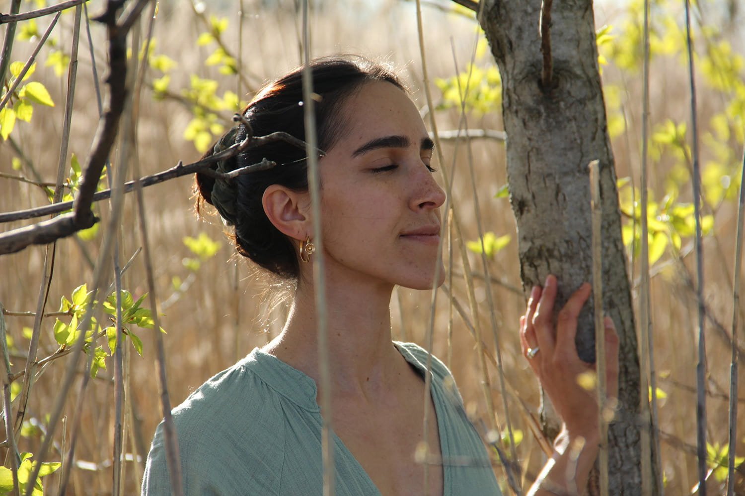 Jil Bianca with eyes closed by a tree, illustrating her offerings in movement, breathwork and 1:1 counseling.