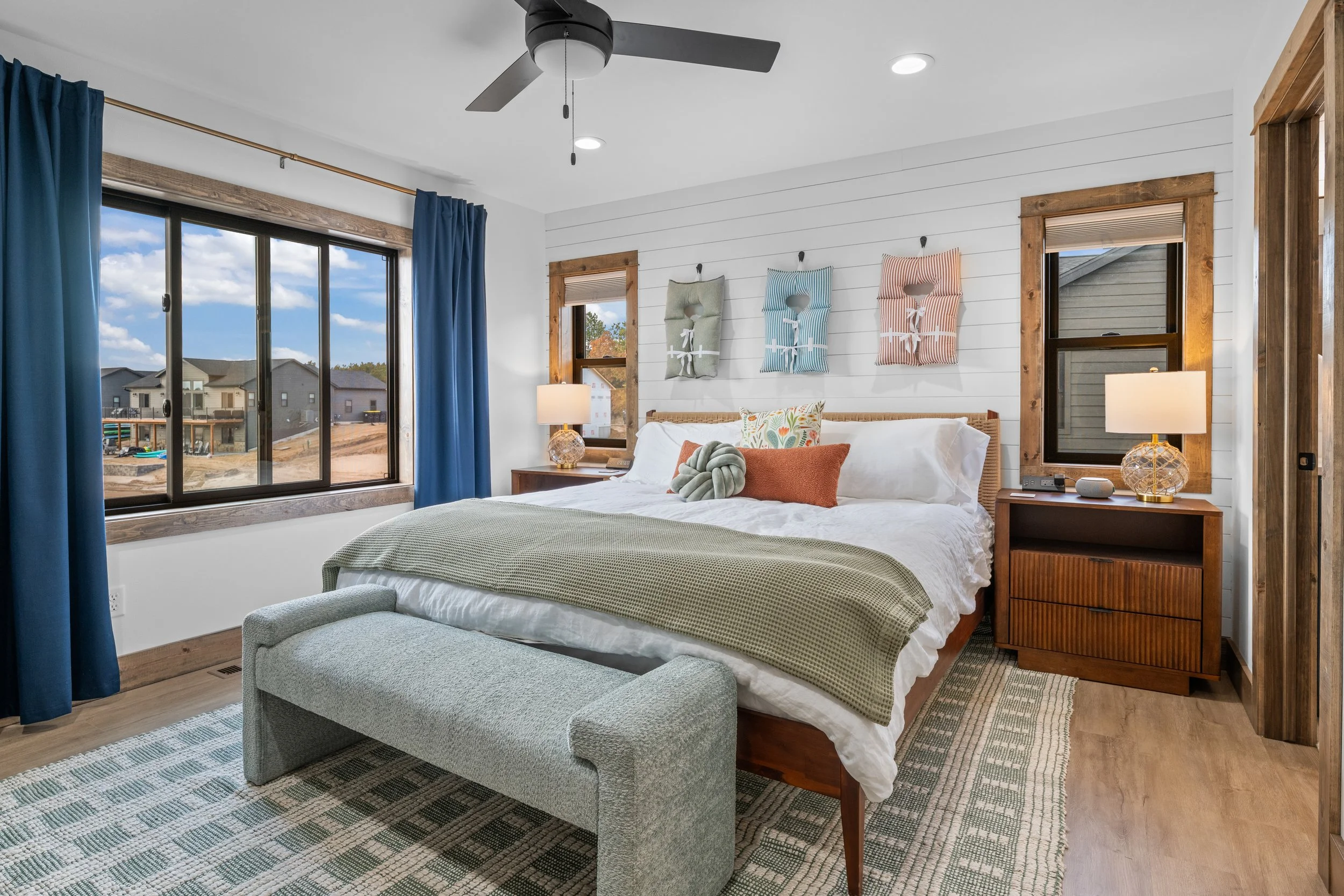 Living room with white walls, light-colored furniture, black and white rug, wall art of Indianapolis city skyline, and a kitchen with gray cabinets and wooden bar stools.