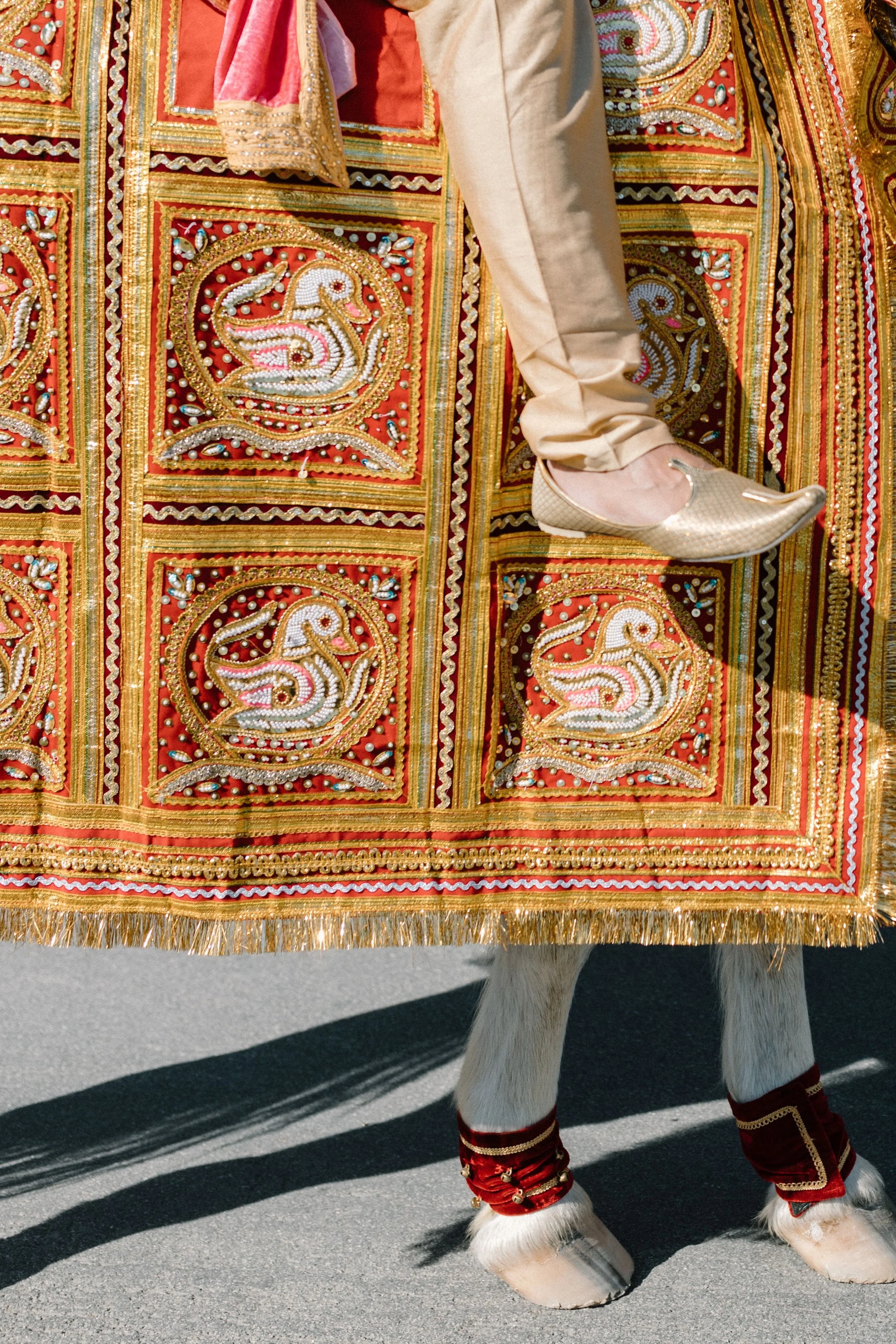 A person dressed as a traditional Indian decorative horse for a parade or festival, with embroidered and beaded designs, and wearing ornate footwear and leg decorations.