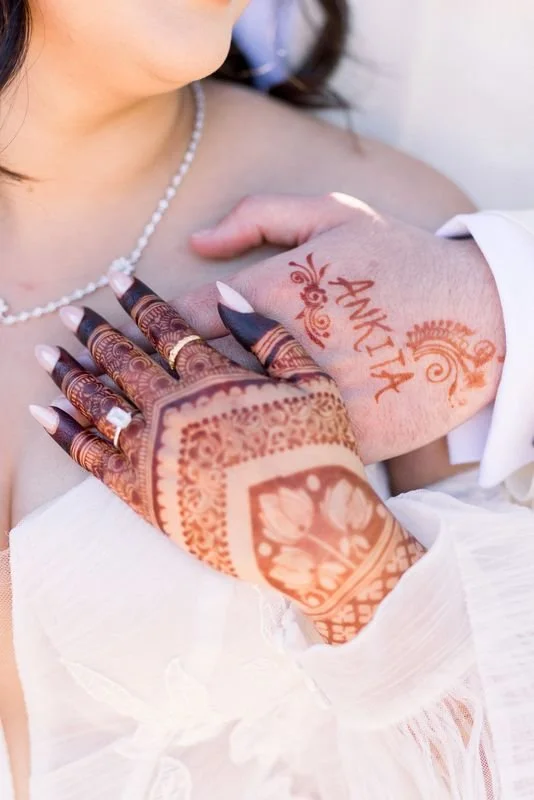 A woman with henna tattooed hands touching a man's chest, who has a henna name and design on his hand.