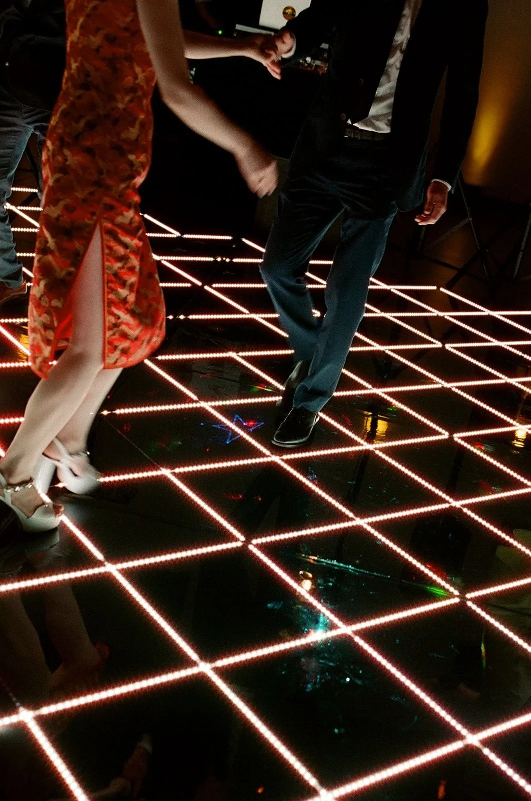 People dancing on a lit-up dance floor with red and white grid patterns.