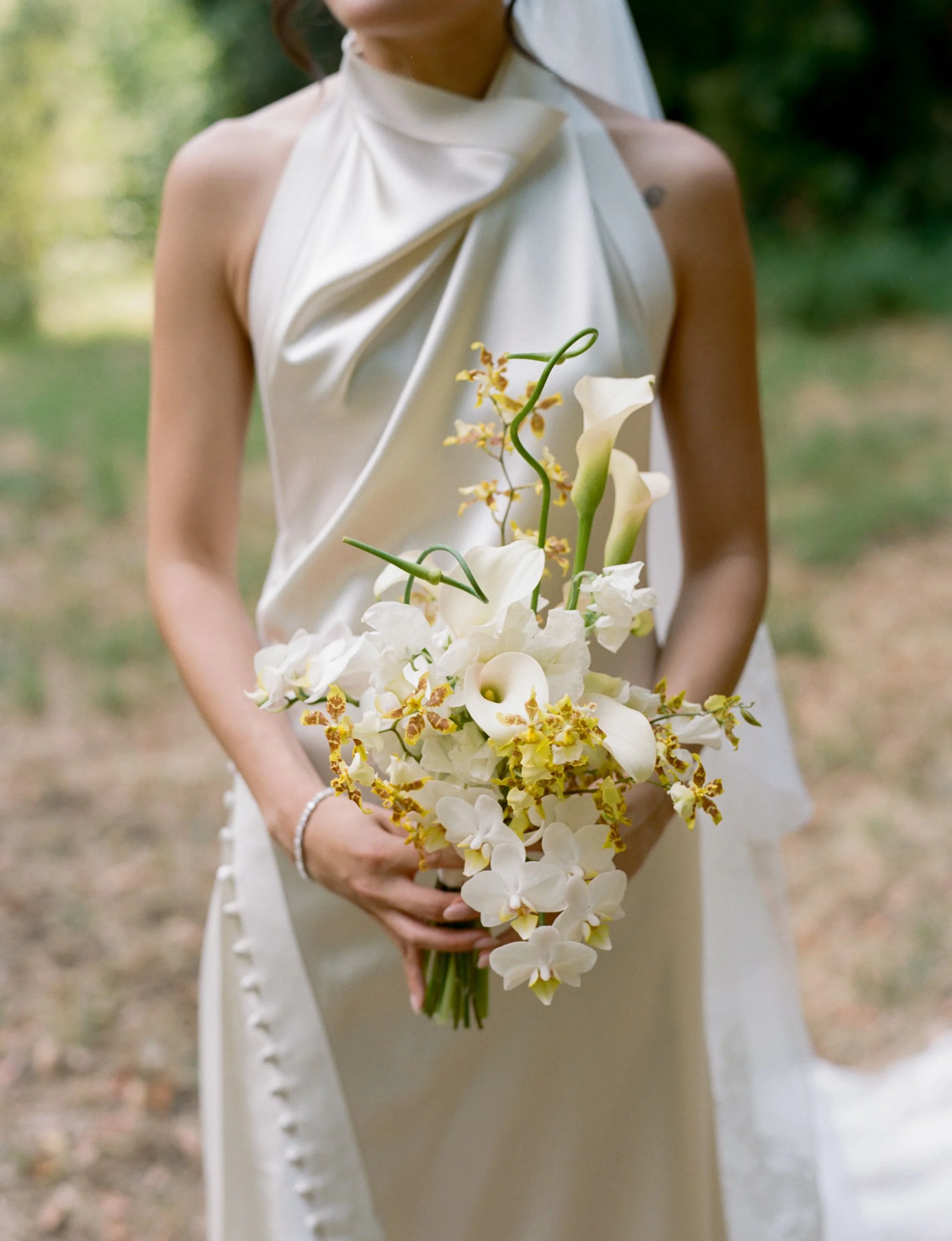 A woman in a white dress holding a bouquet of white and yellow flowers outdoors.