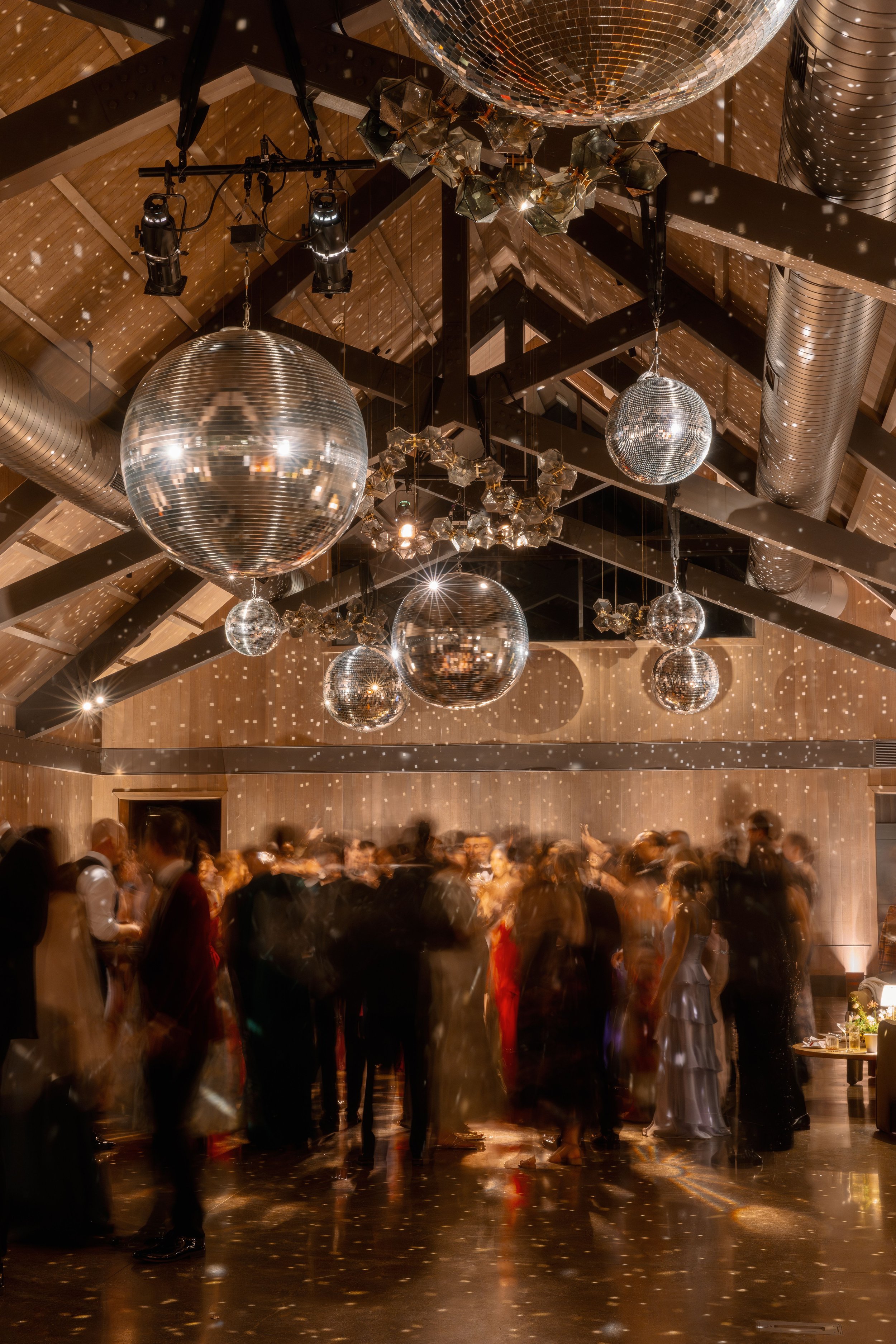 People dancing at a party or event with disco balls hanging from the ceiling.