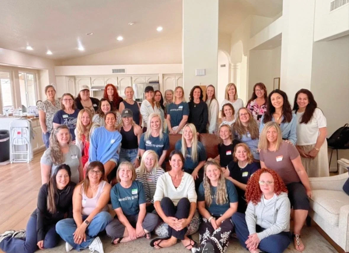 A large group of women gathered in a spacious, well-lit living room, posing for a group photo during a social or professional event.
