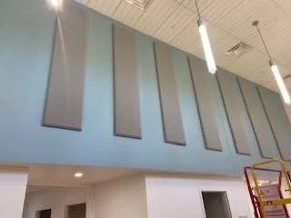 Image shows a teal wall with gray sound panels and one hanging light