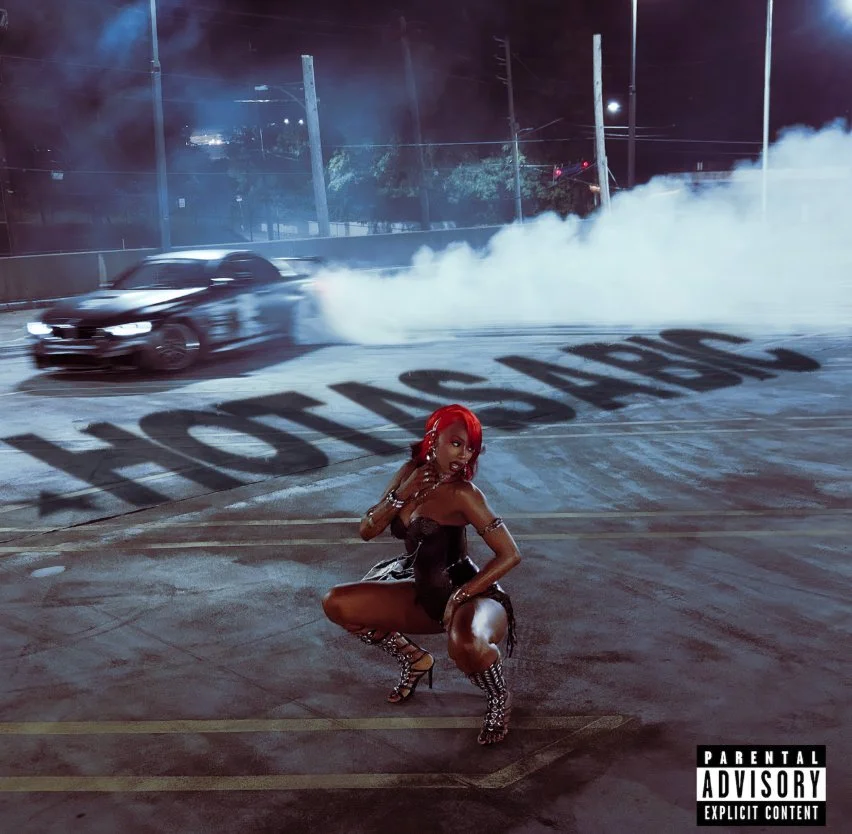 Flo Milli "Hot As A Bic" single artwork featuring the artist with red hair crouching in a black leather outfit on a car park at night with a drifting car and smoke in the background