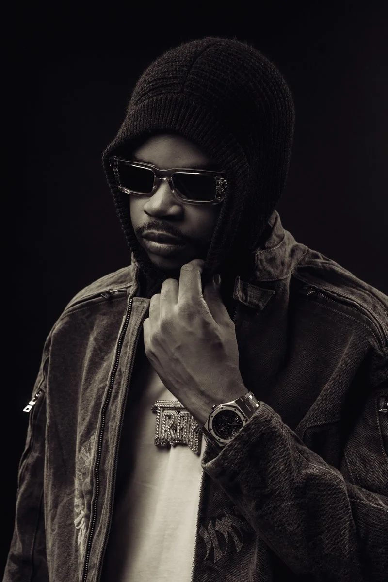 Press shot of rapper K-Trap wearing sunglasses, beanie hat and denim jacket with diamond chain and luxury watch, black and white studio portrait