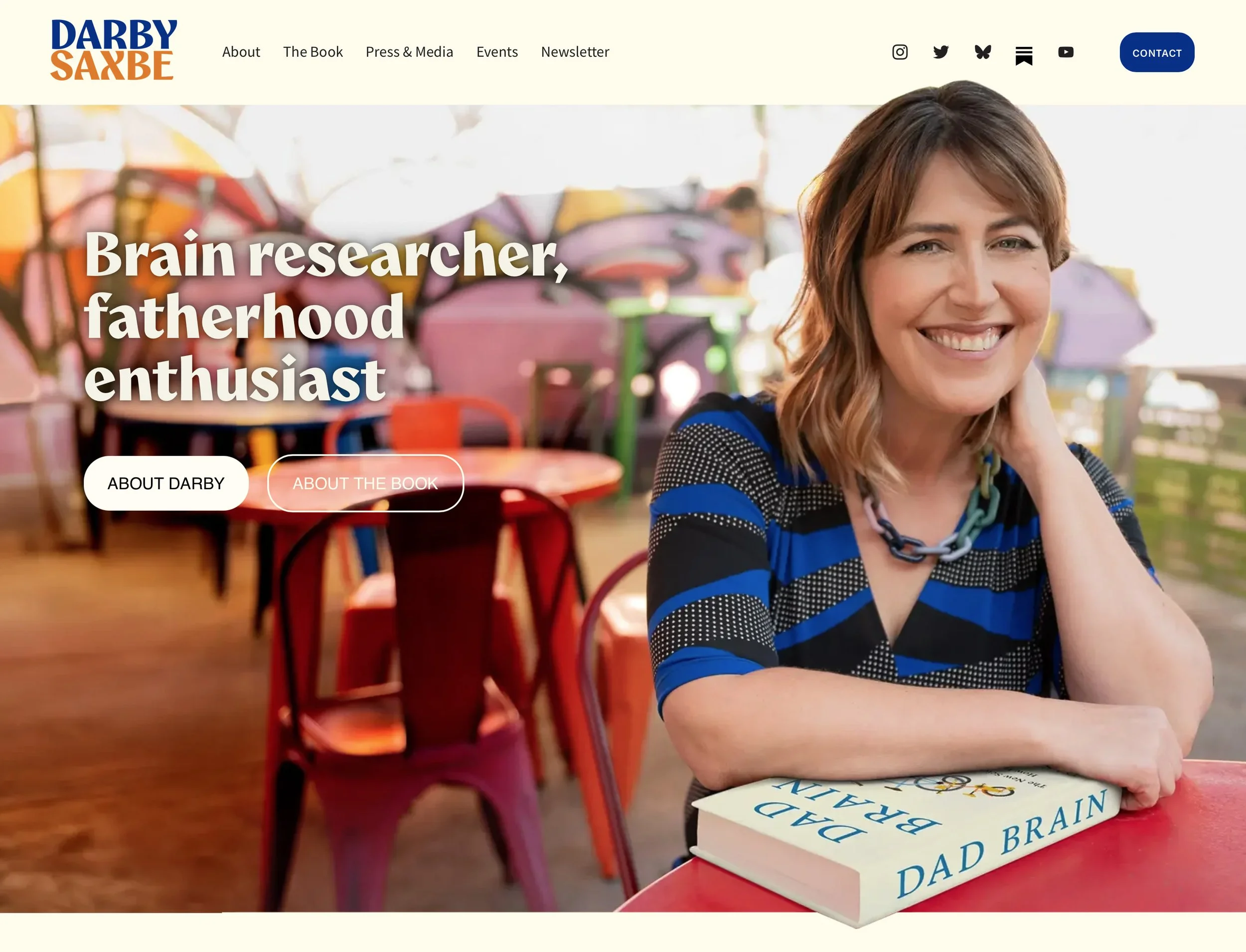 Darby Saxbe's website homepage with the headline "Brain researcher, fatherhood enthusiast" over a photo of her smiling at a red cafe table with her book Dad Brain.