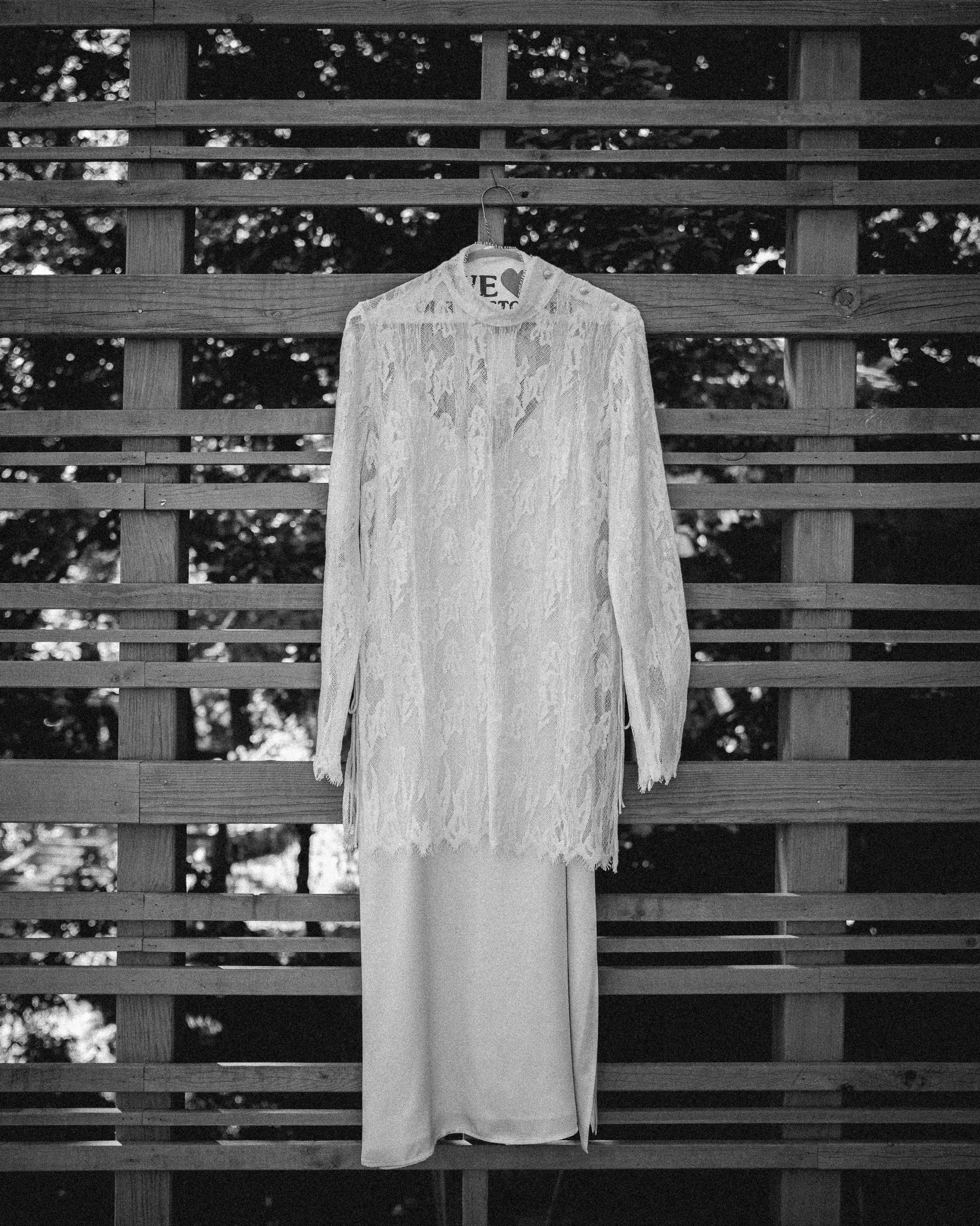 A vintage lace wedding dress hanging on a wooden lattice against trees in the background.