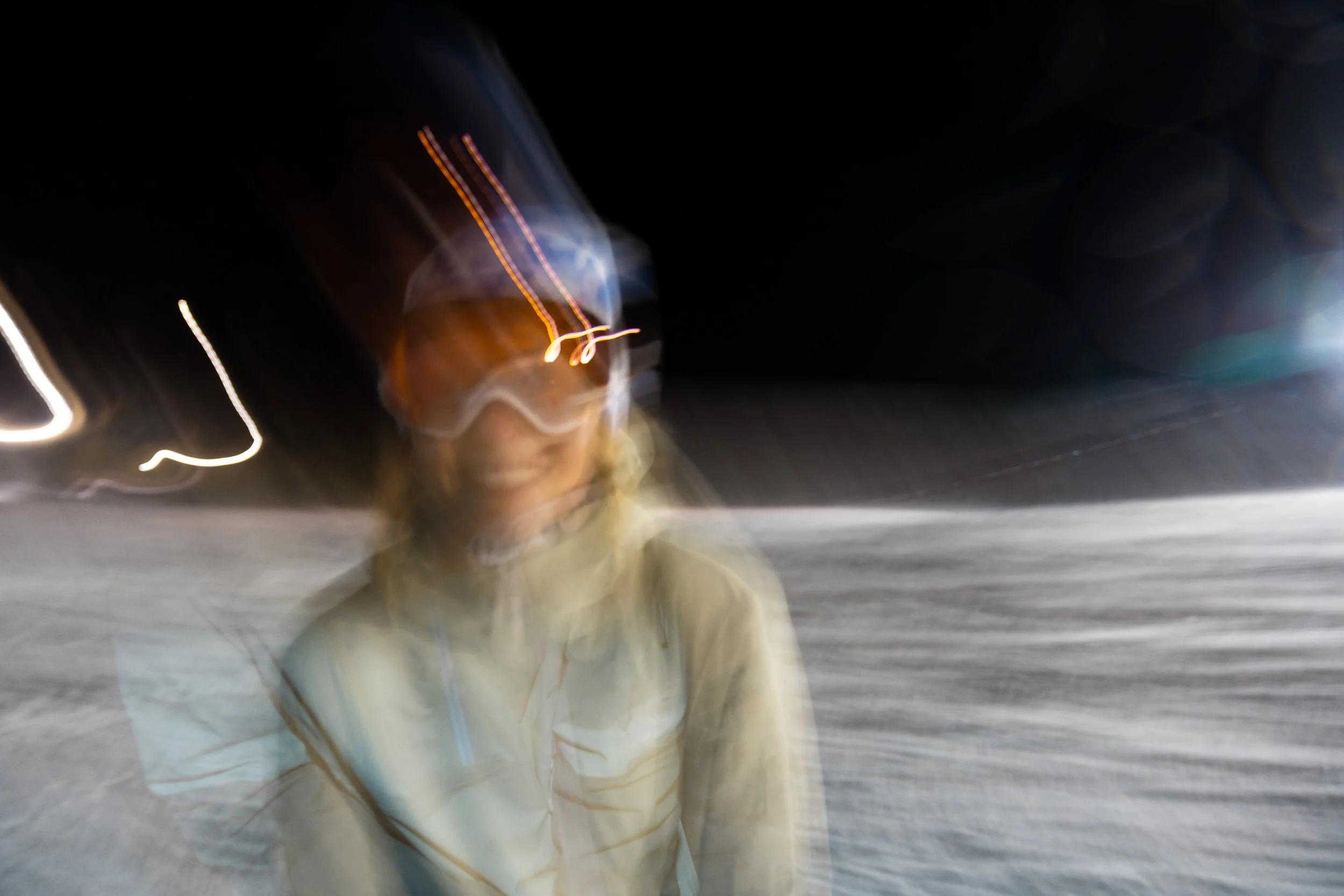 Blurred photo of a person in a jacket at night with light trails in the background.