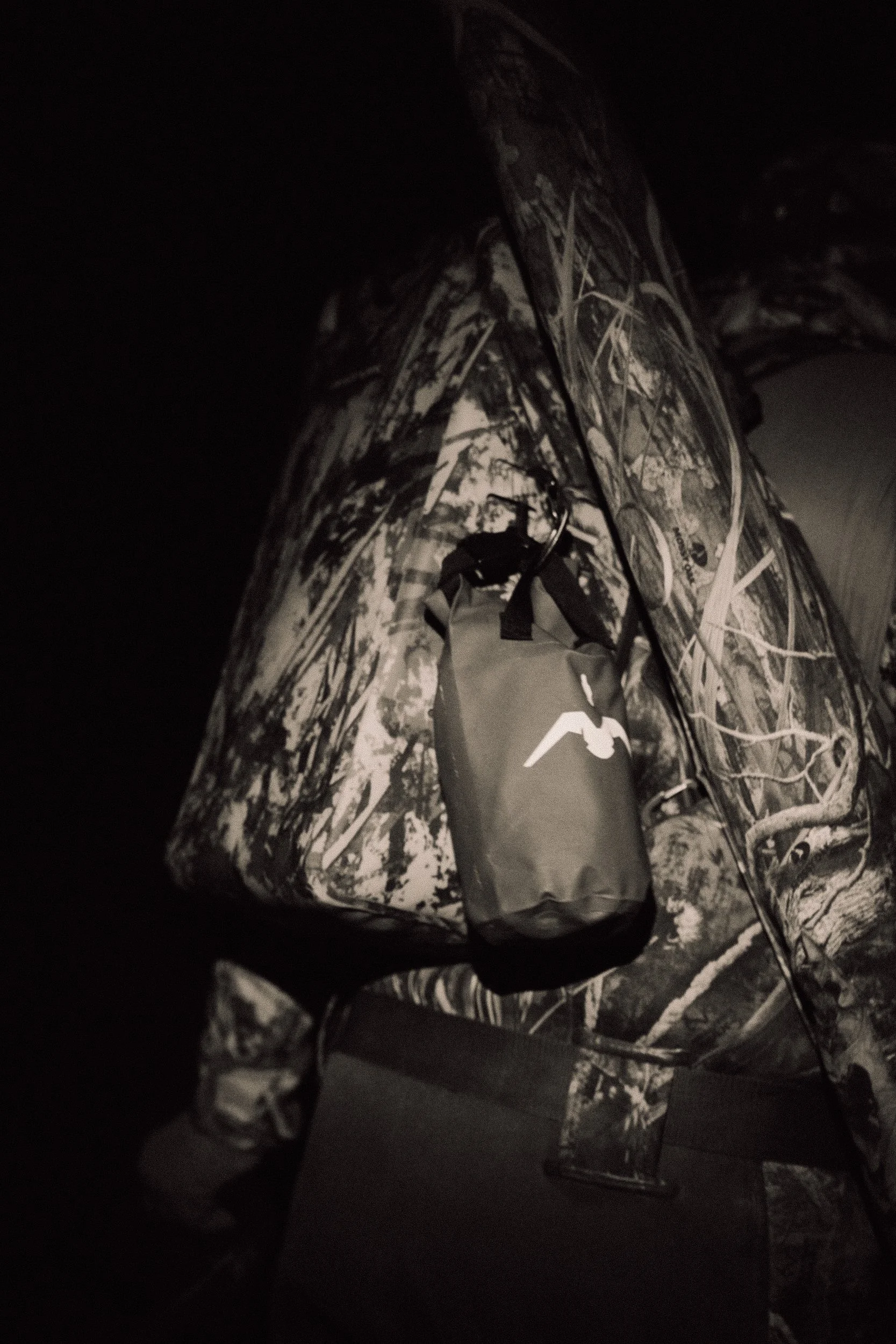 A camouflage-patterned bag with a small black waterproof pouch attached, resting on a surface.