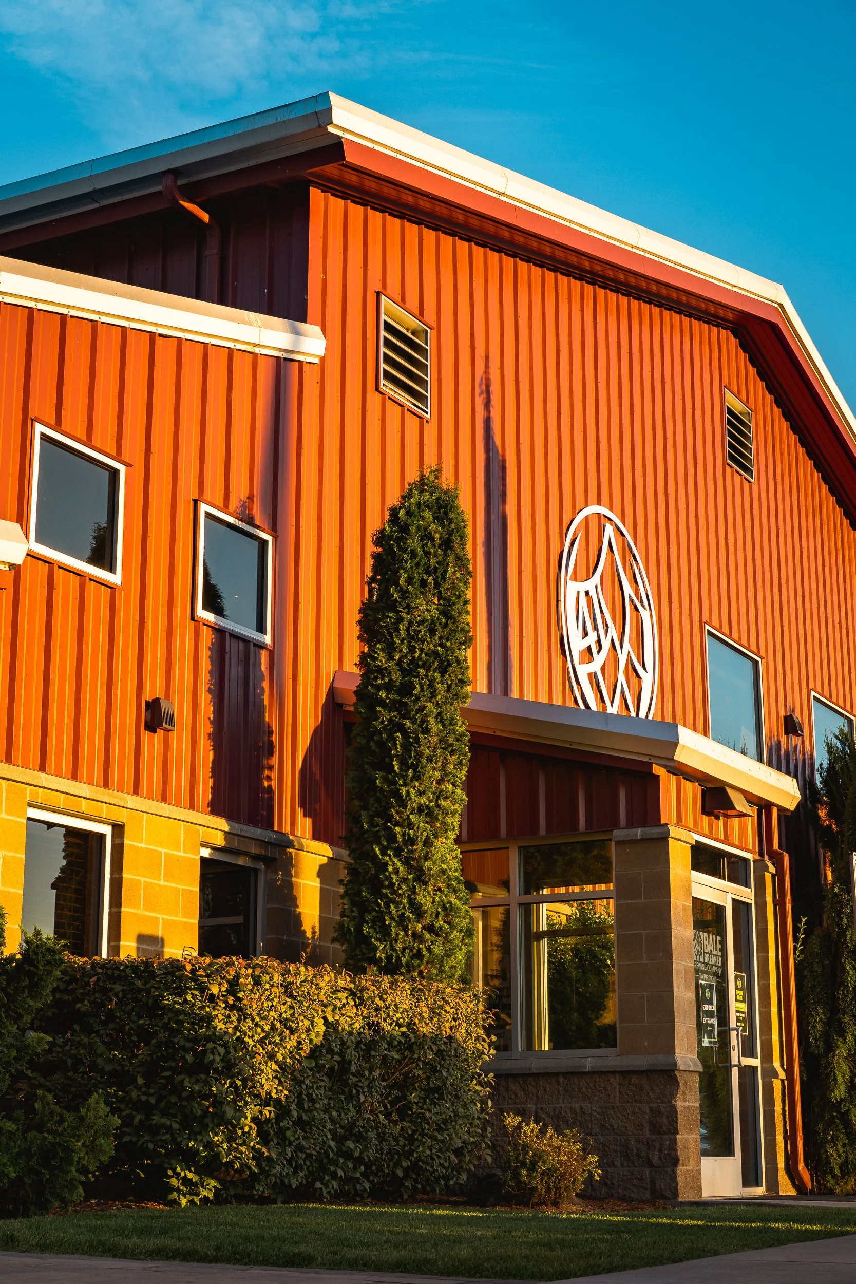 Photo of a red barn-style building with a large logo on the front, surrounded by greenery and illuminated by sunset light.