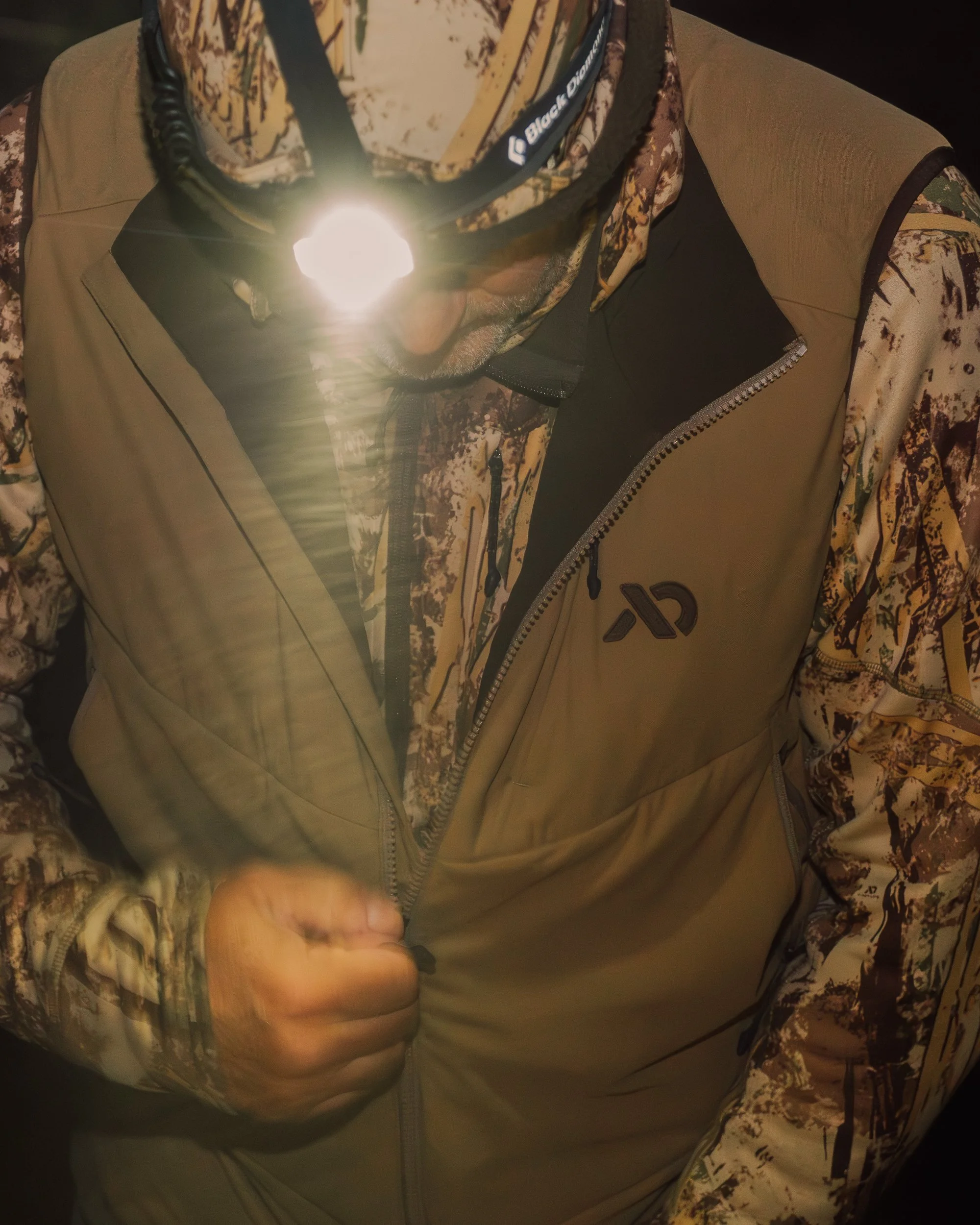 A person in camouflage outdoor clothing and a headlamp.