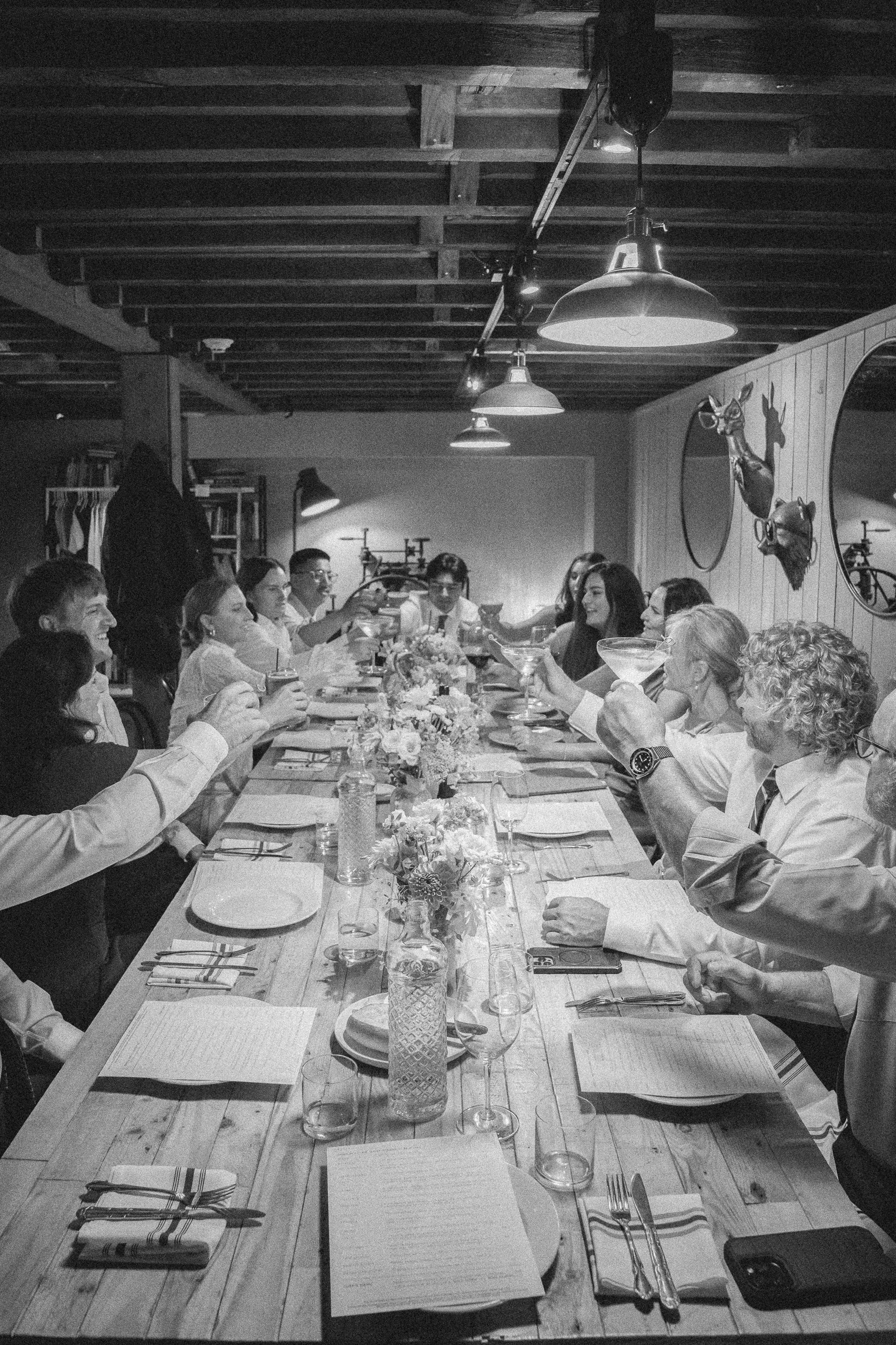 People gathered around a long dining table in a rustic restaurant, holding up glasses for a toast and smiling.