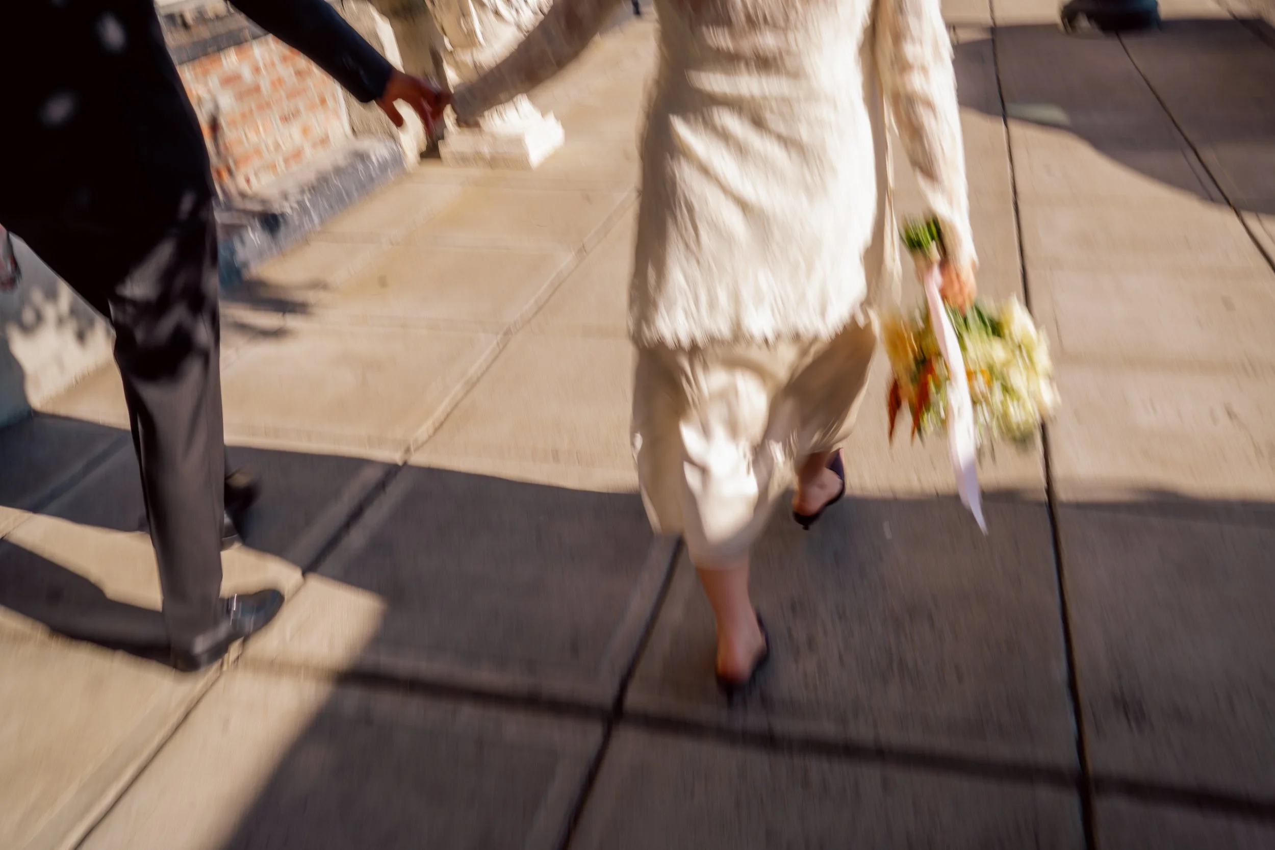 A person dressed in a white outfit walking on a sidewalk while holding a bouquet of flowers.
