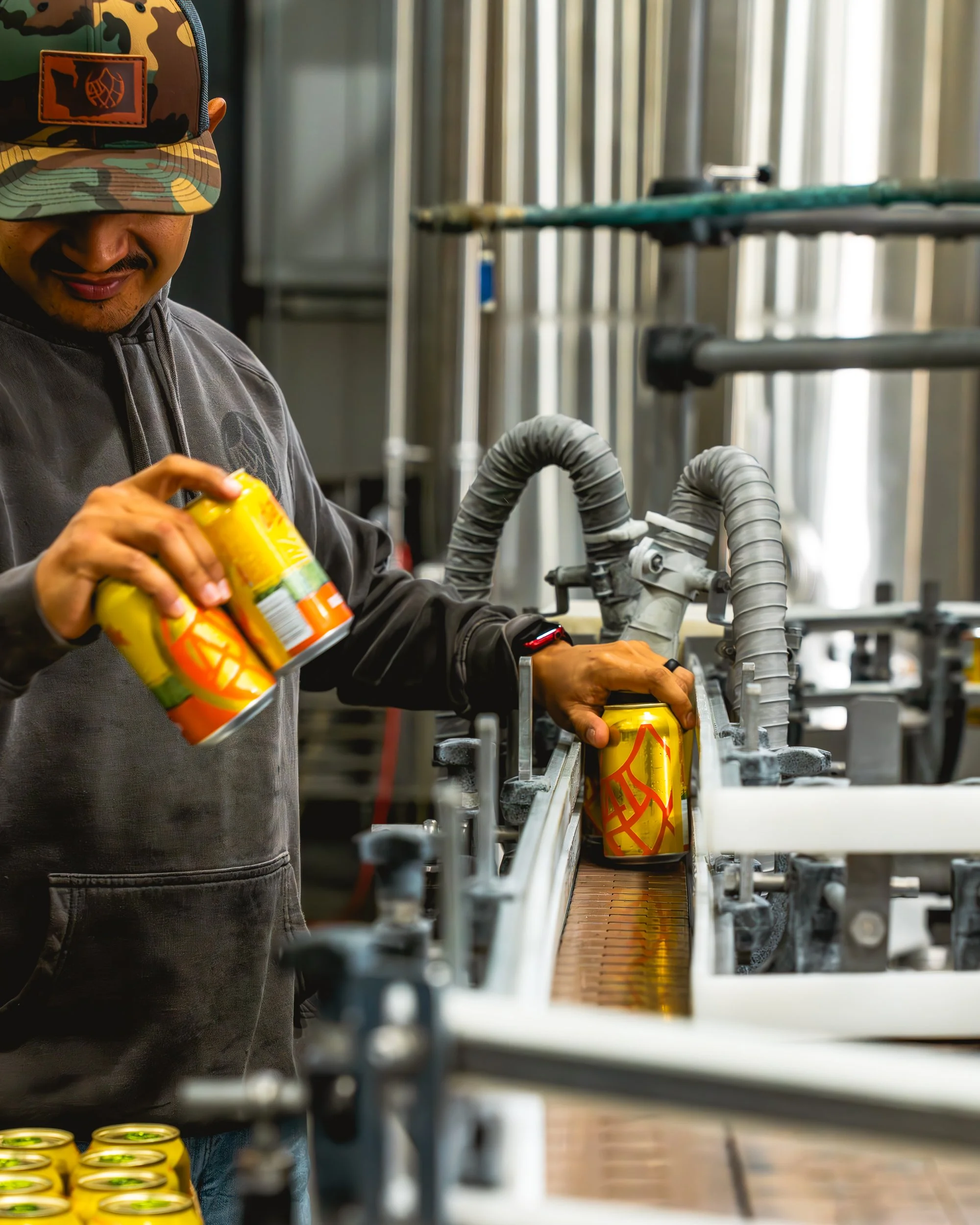 A worker shows a man how to fill cans of soda on a production line in a factory.