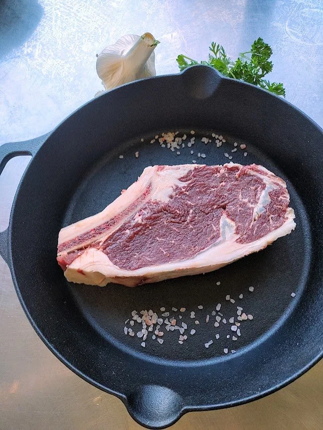 Raw steak in cast iron skillet with garlic and parsley