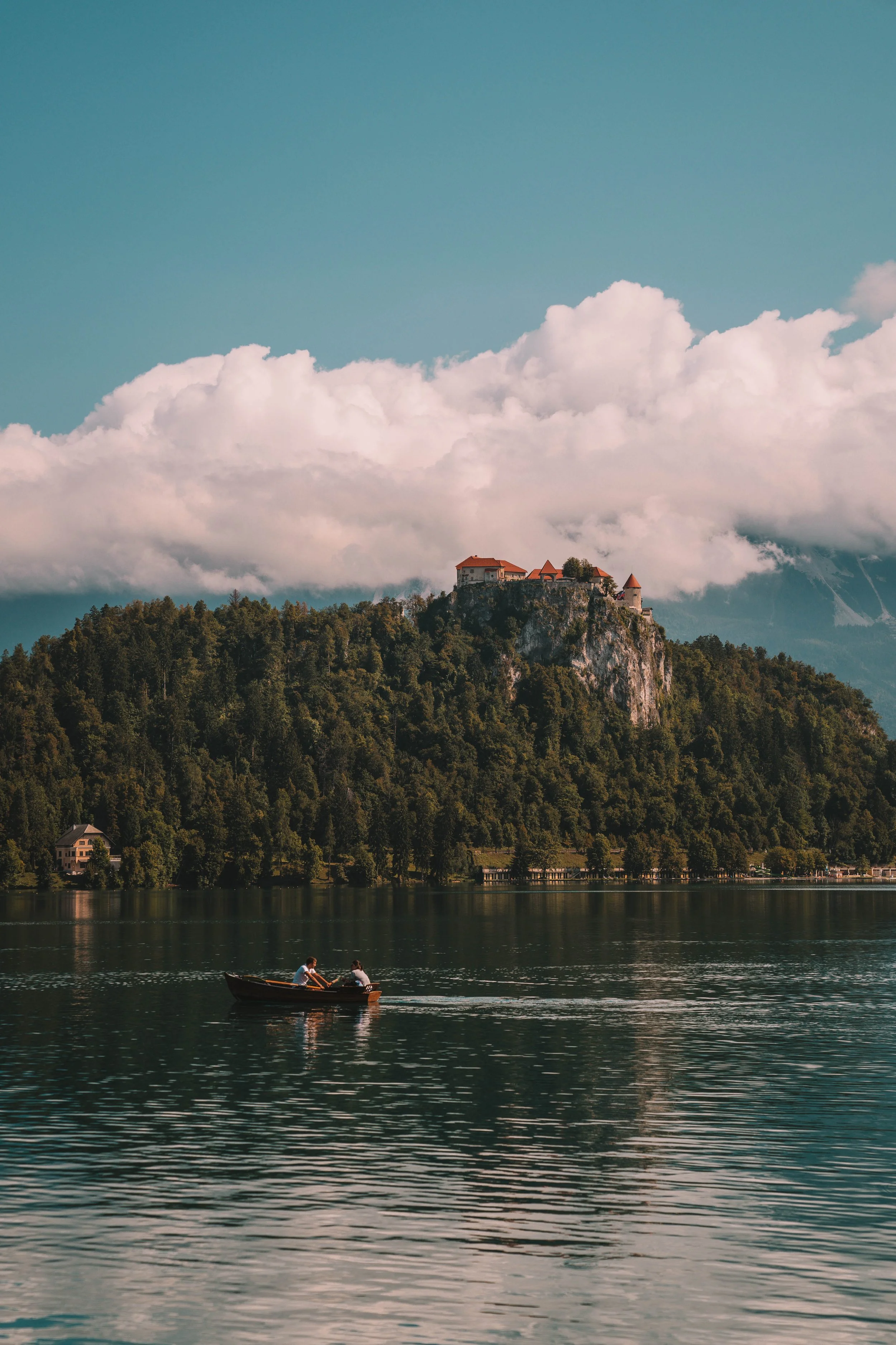 Scenic view of a castle on a hill with lush forest, lake, and boaters