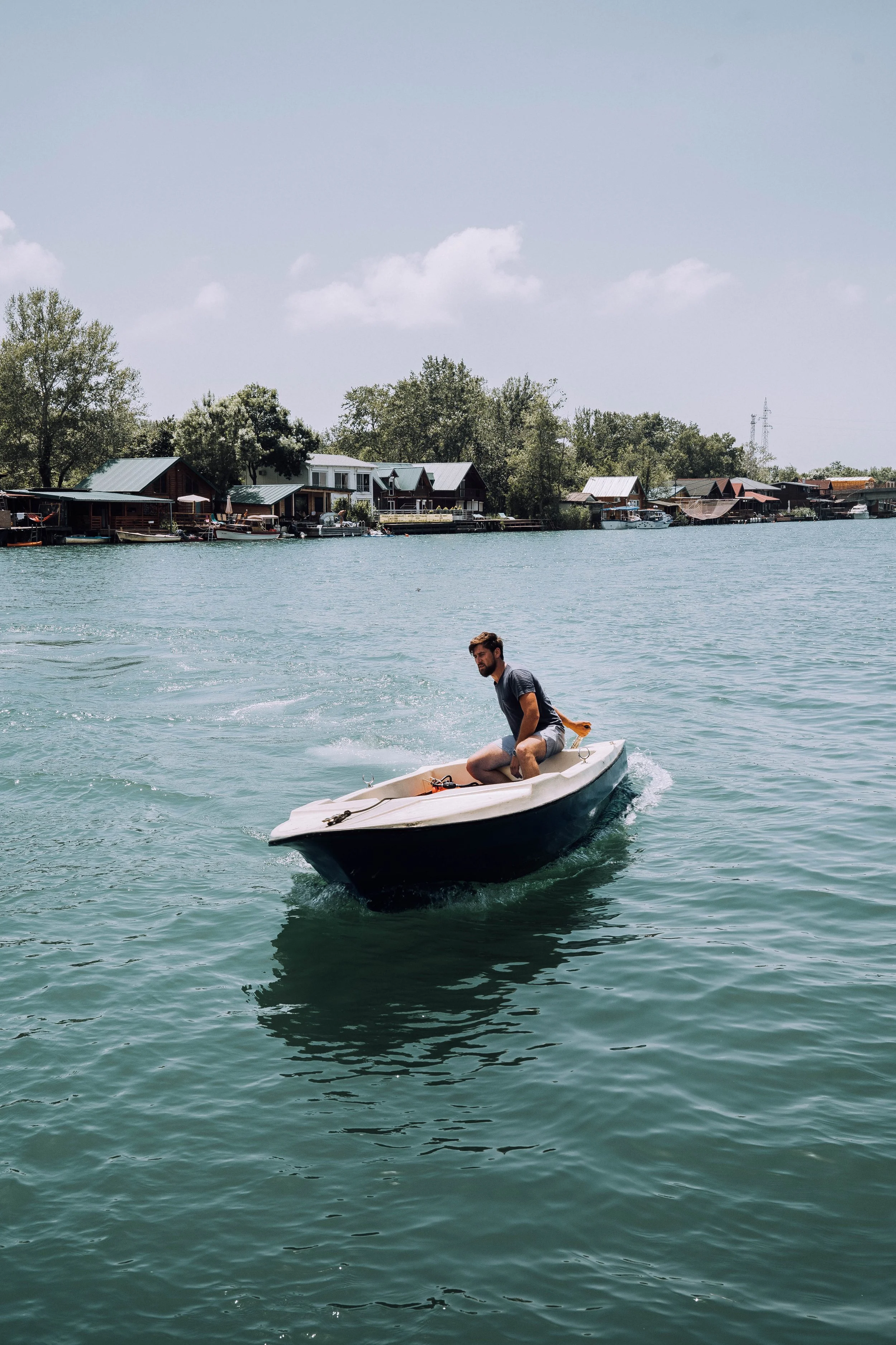 Man in a small motorboat on a lake with houses and trees in the background.