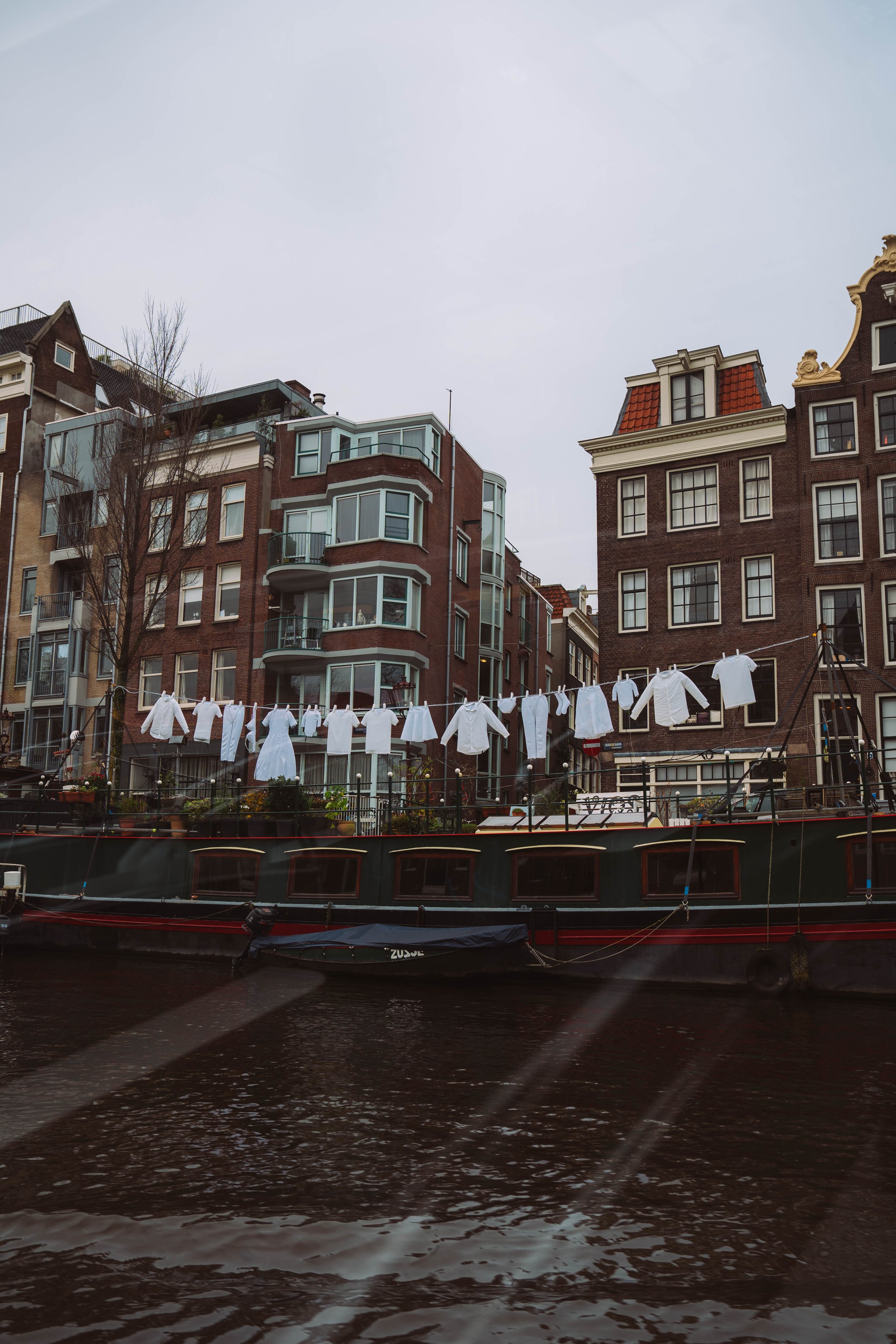 Canal in Amsterdam with clothes hanging on a line, surrounded by traditional Dutch buildings and a houseboat.