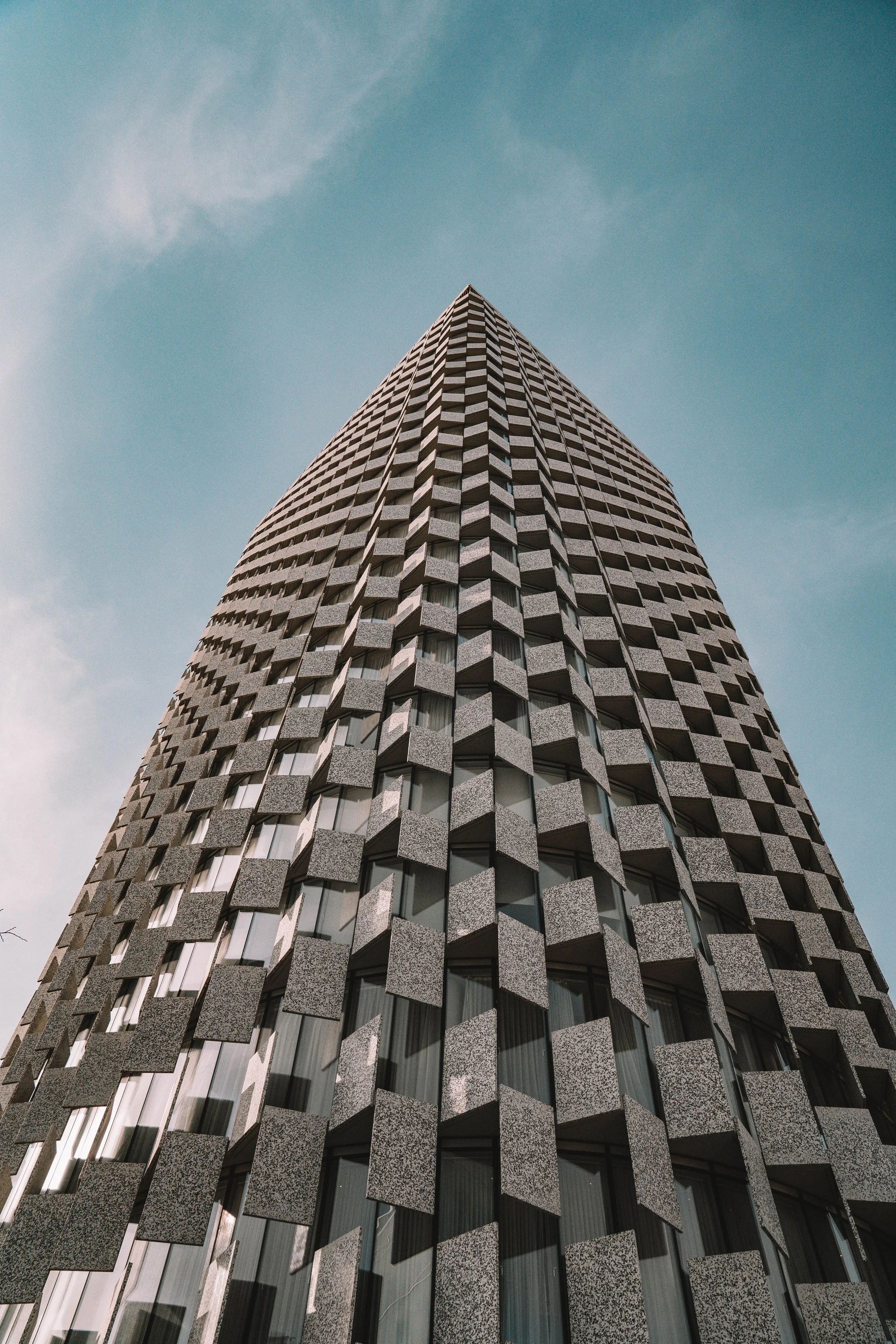Low angle view of a tall building with a unique checkered facade against a blue sky.