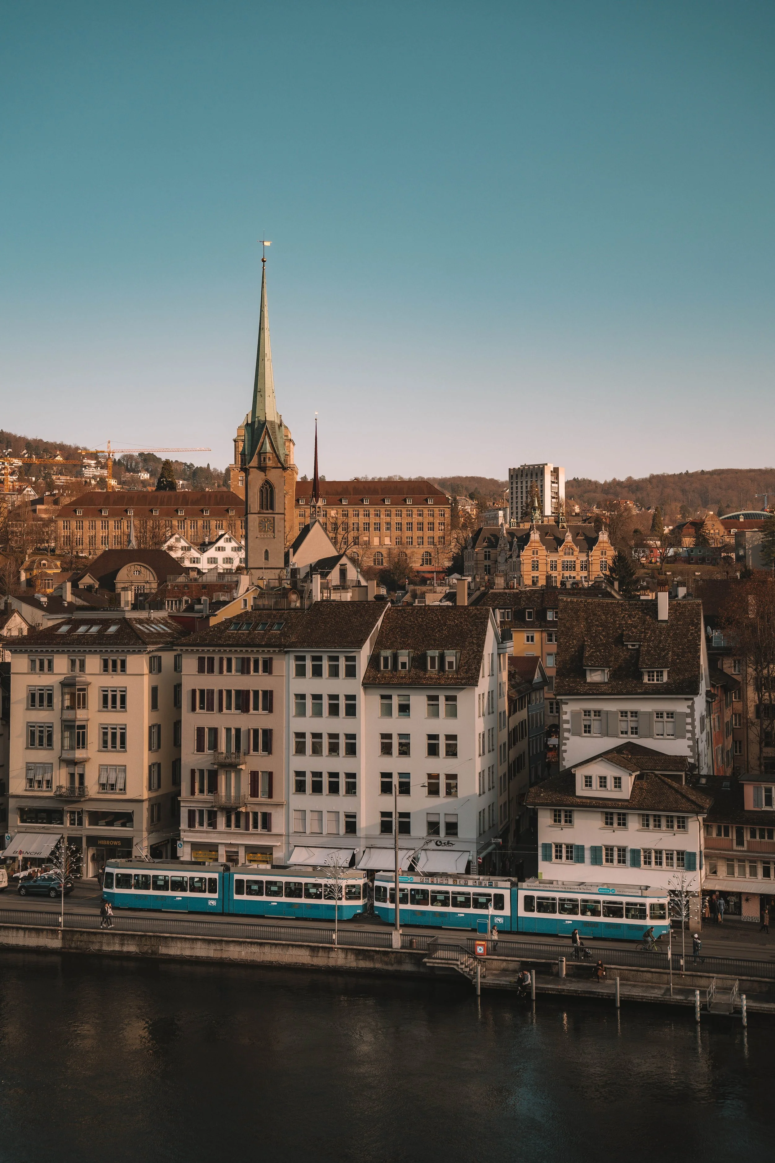 Cityscape featuring historic church tower, buildings, tram, and river.