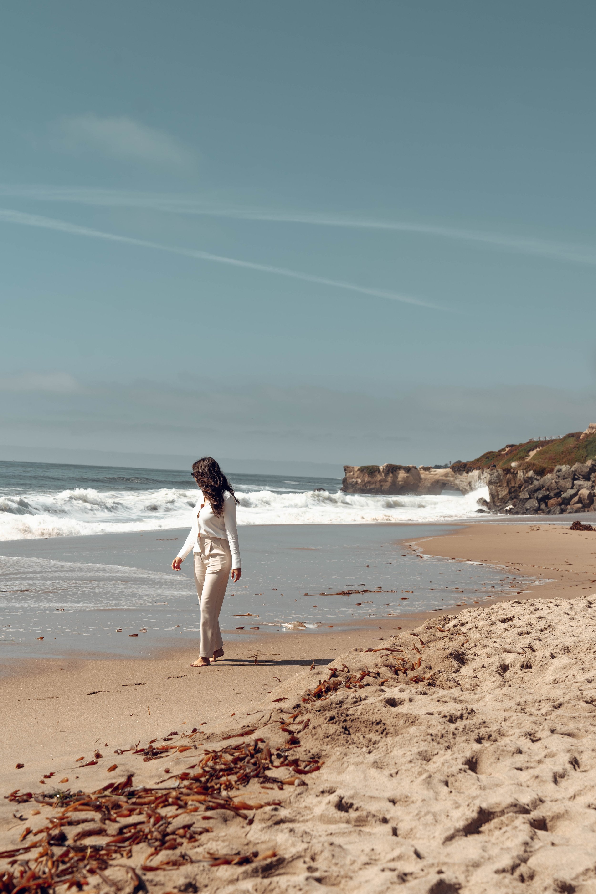 Person walking on a sandy beach with ocean waves and clear sky in the background. California