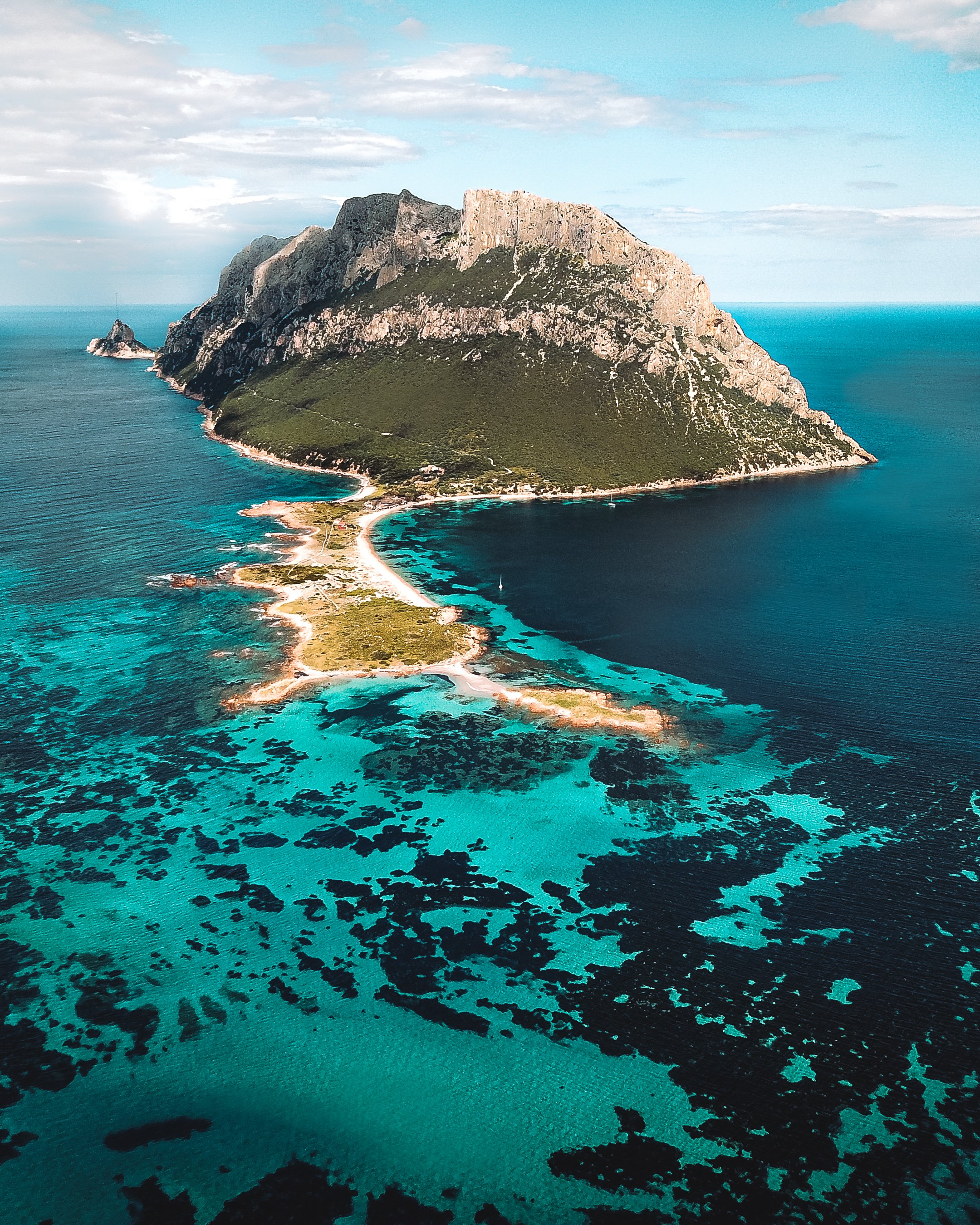 Albanian female photographer photographs Aerial view of lush green mountain island with rocky cliffs surrounded by turquoise sea and coral reefs.