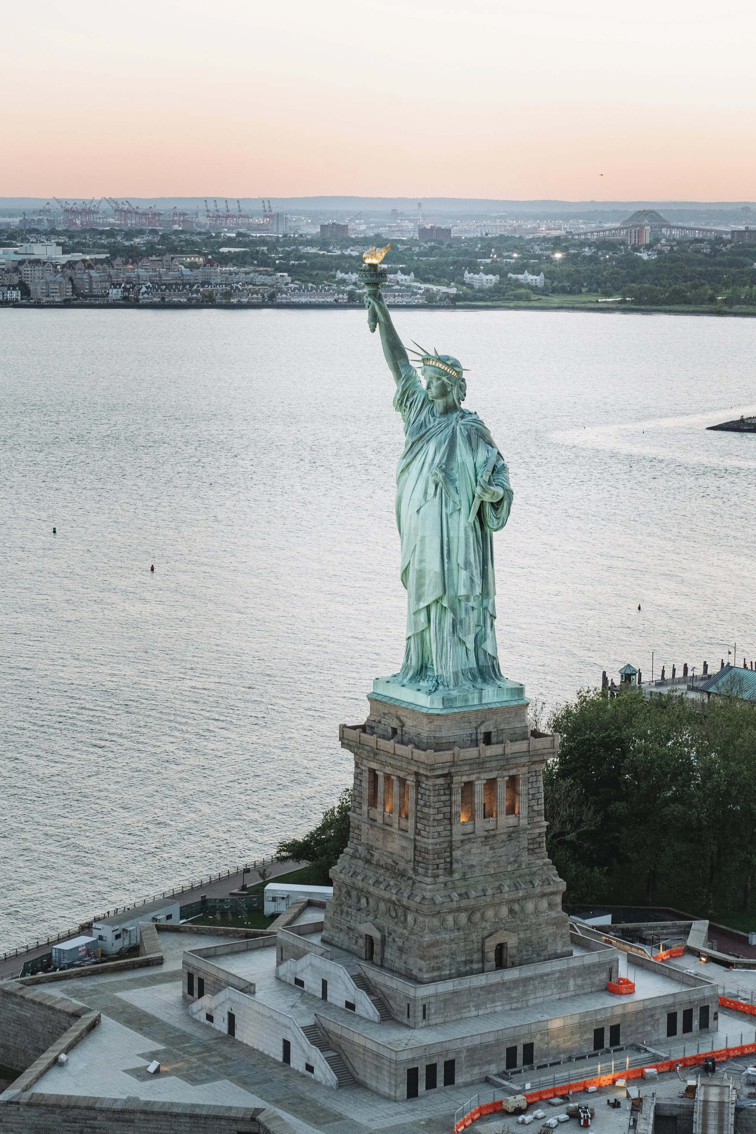 Statue of Liberty on Liberty Island with distant view of New Jersey in the background, at sunset.