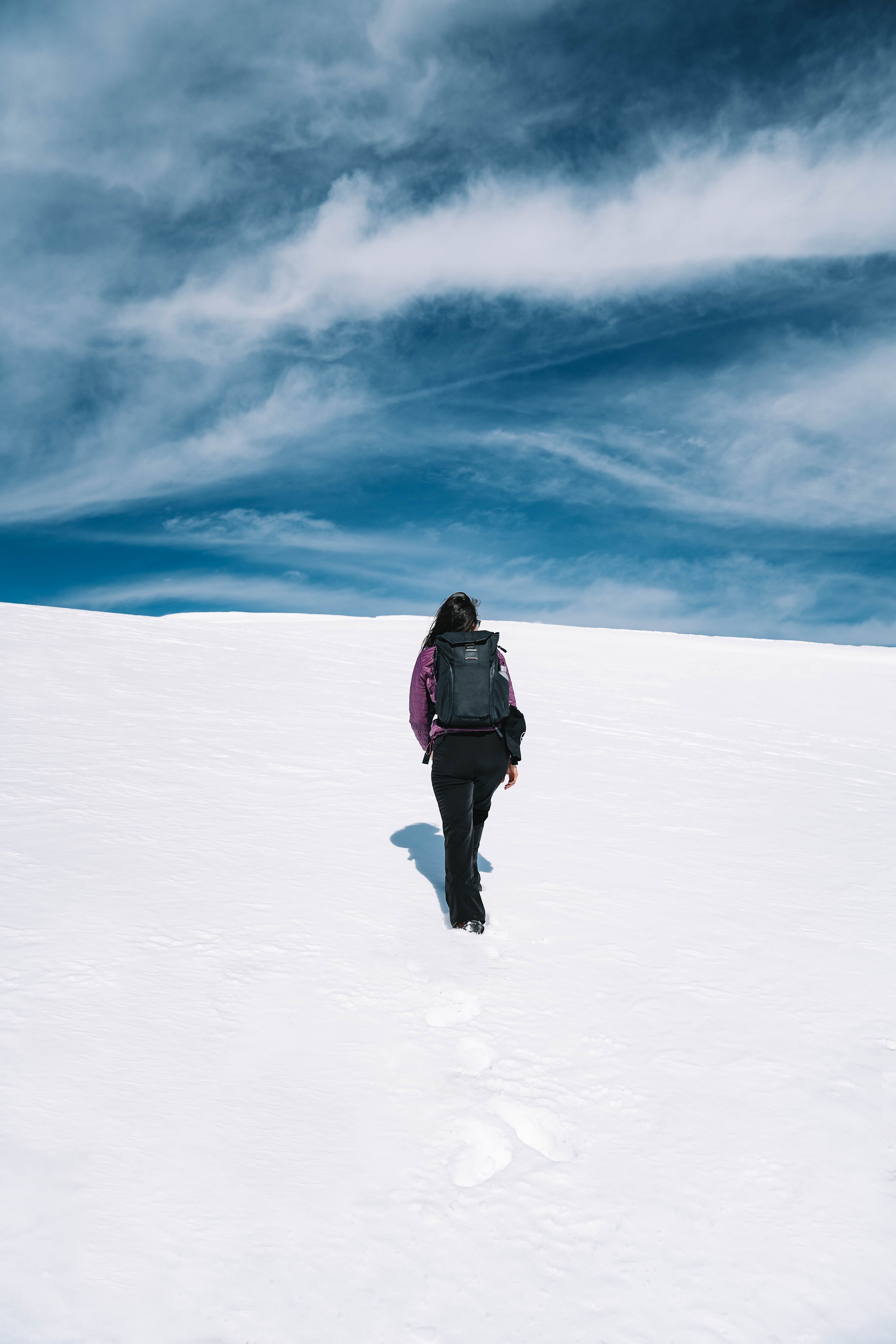Person with backpack walking on snow under a blue sky with clouds.